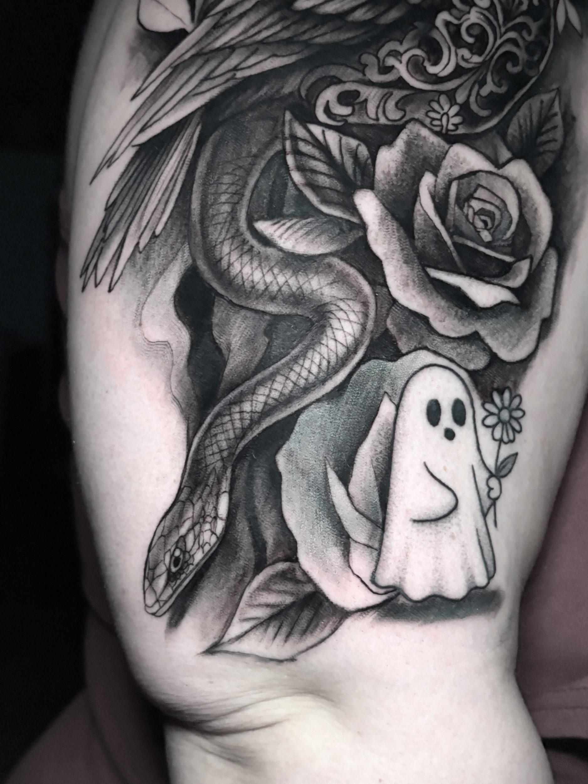 A black and gray tattoo featuring a woman's face with a flower in her hair, a rose, a snake, and various decorative elements.