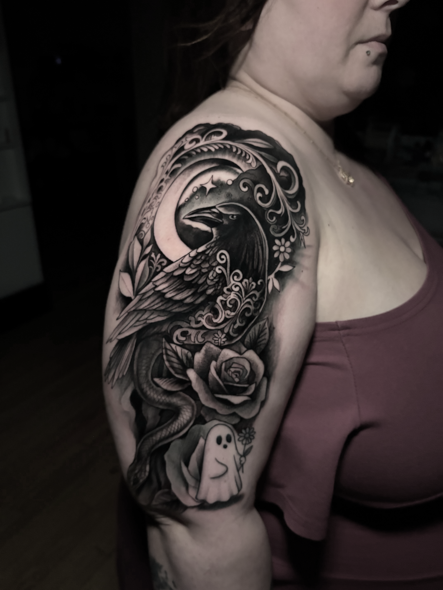 A person with a sleeve tattoo featuring a bird, snake, flowers, and a moon on their upper arm.