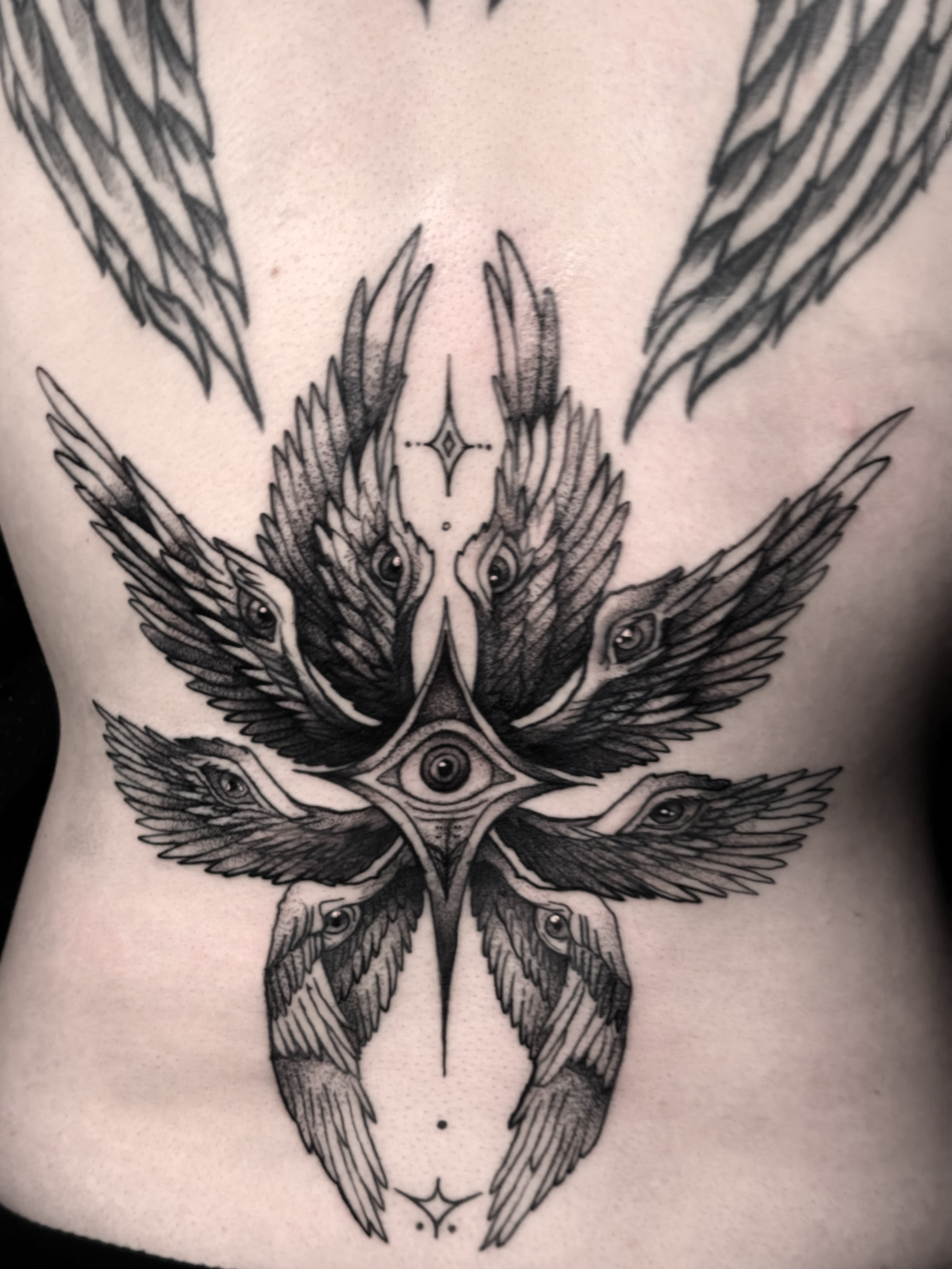 Black and gray tattoo of a symmetrical bird with multiple eyes and intricate patterns covering a person's chest.