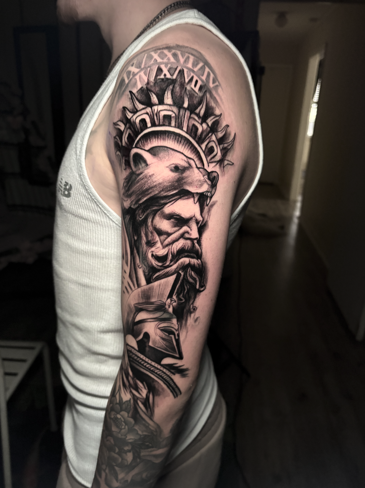 Black and gray tattoo sleeve featuring a wolf and a bearded man with a helmet, Roman numeral clock, and decorative elements.
