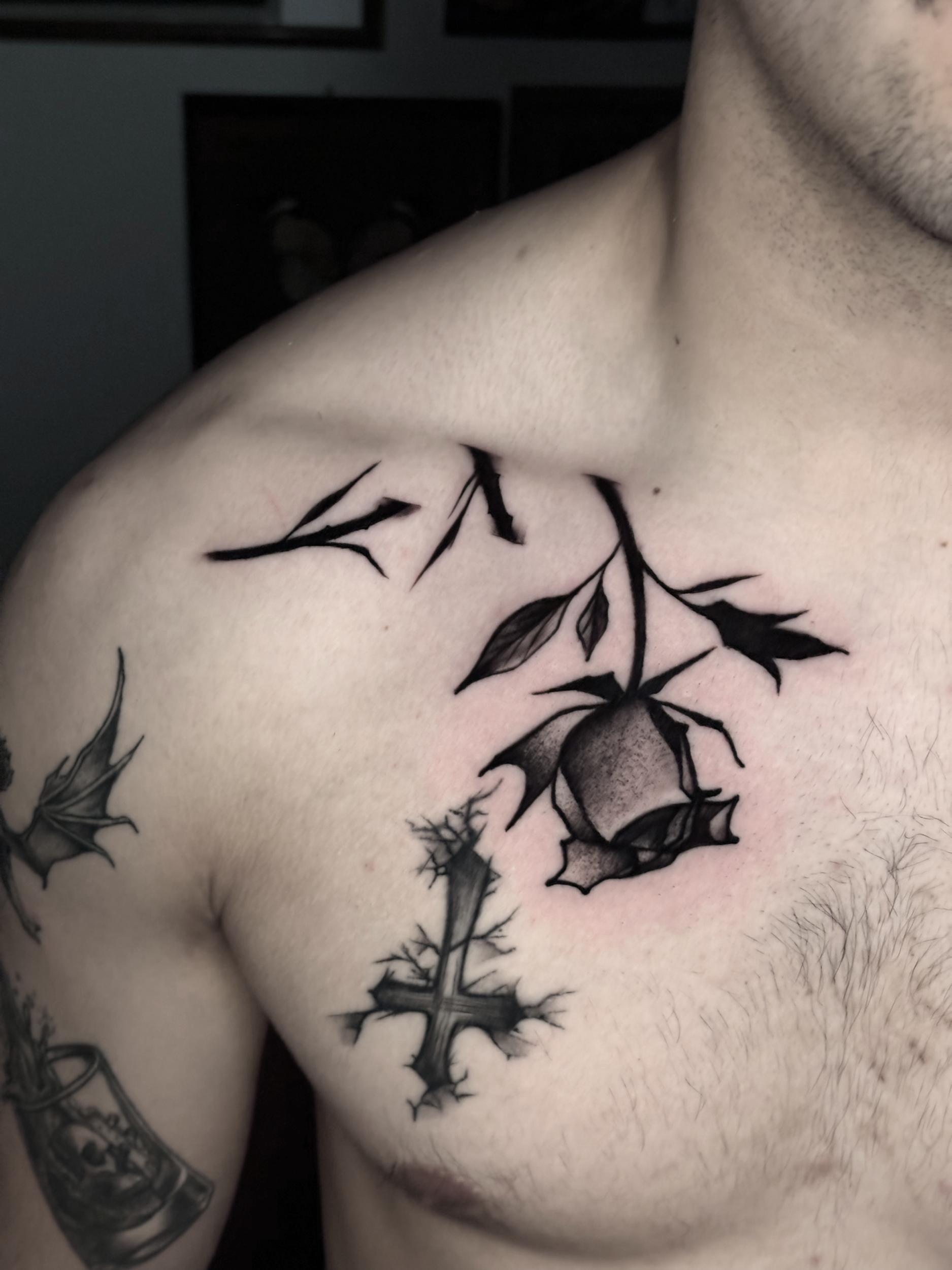 Close-up of a person's chest with multiple black tattoo designs, including leaves and a soda can.