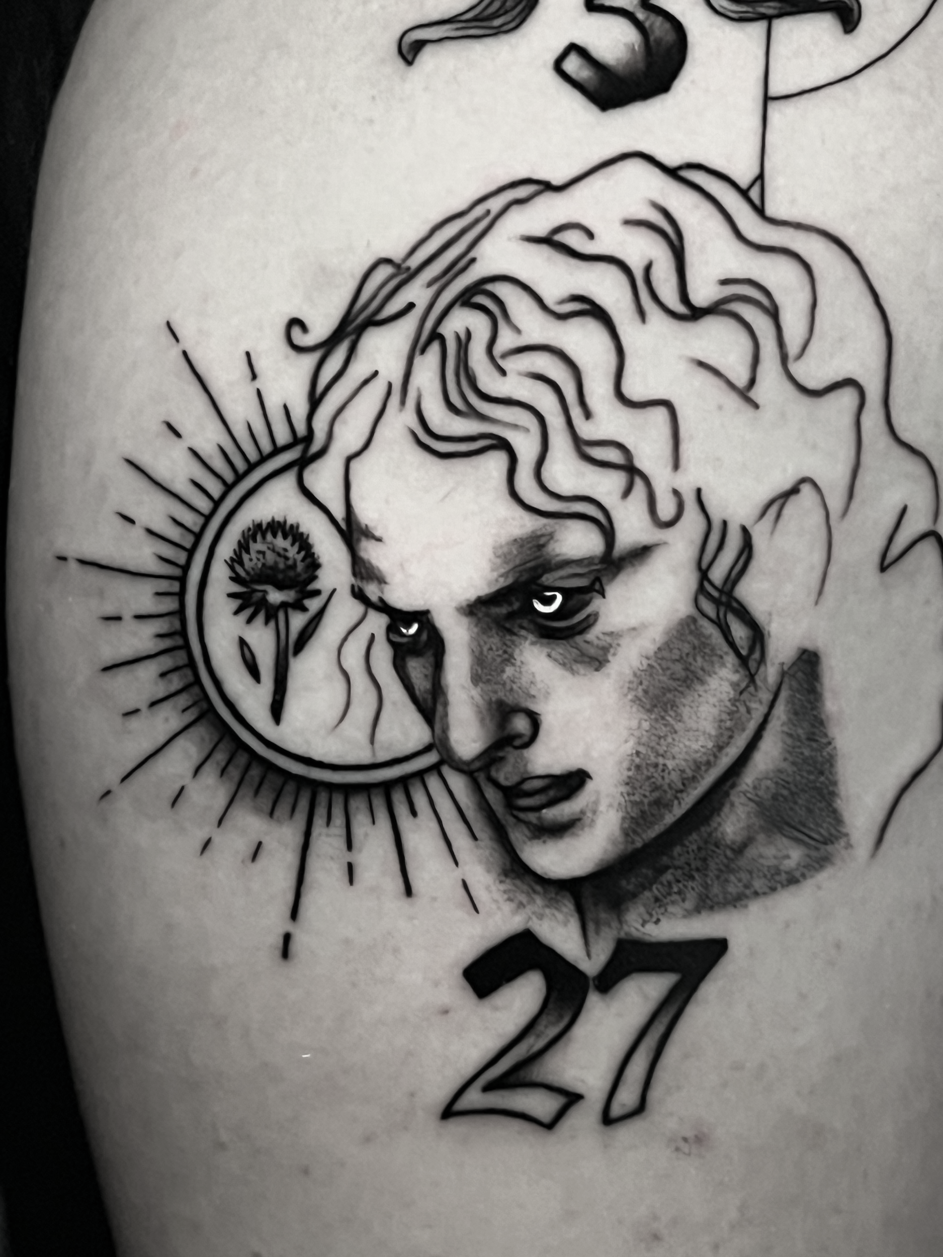 A tattoo depicting a woman's face with closed eyes and long flowing hair, framed by a circular design resembling a sun with rays, on someone's arm.
