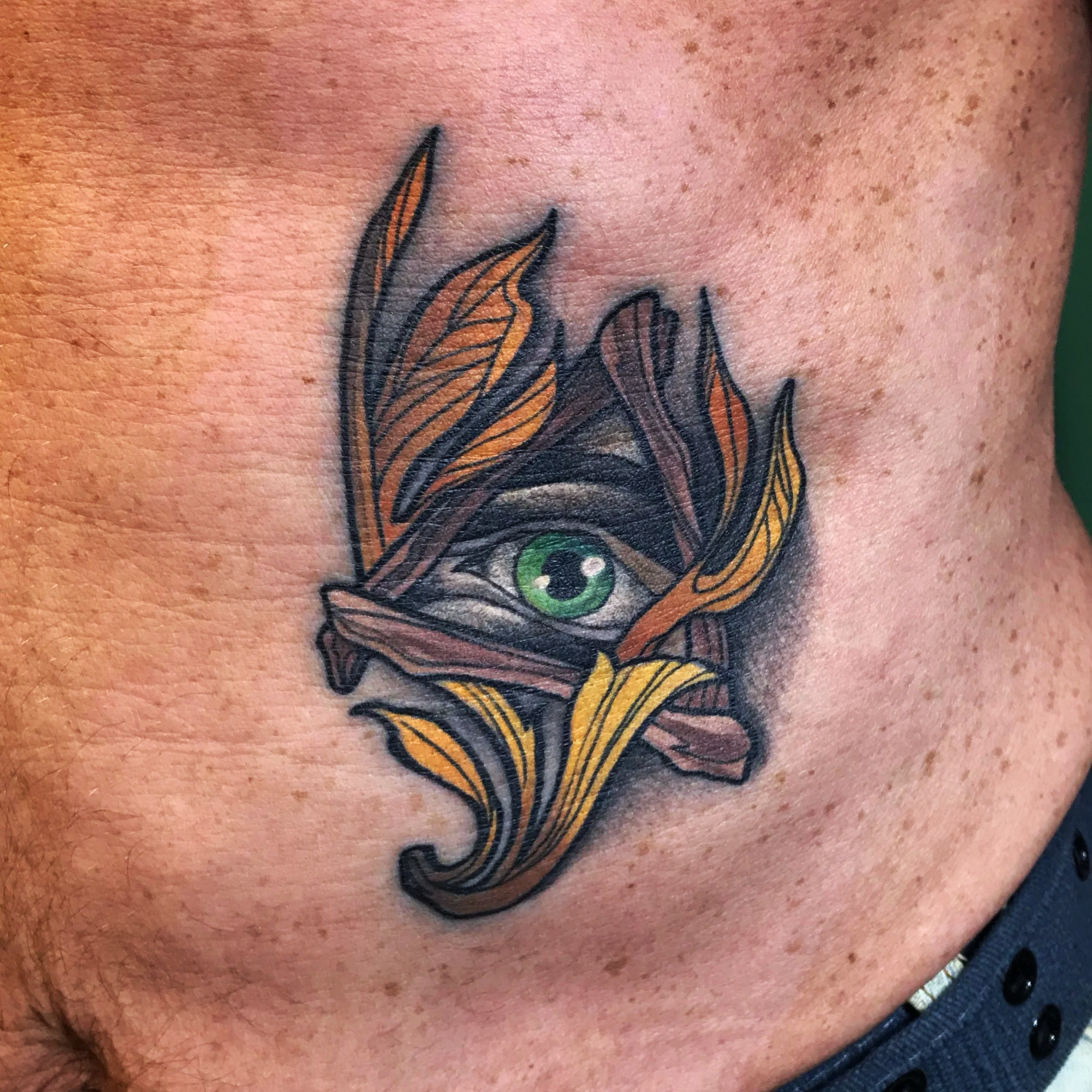 Neo-traditional green eye tattoo framed by flowing ornamental leaves with bold black linework and warm gold tones by Salvador Vargas III, serving Bluffton SC, Savannah GA, and Charleston SC.