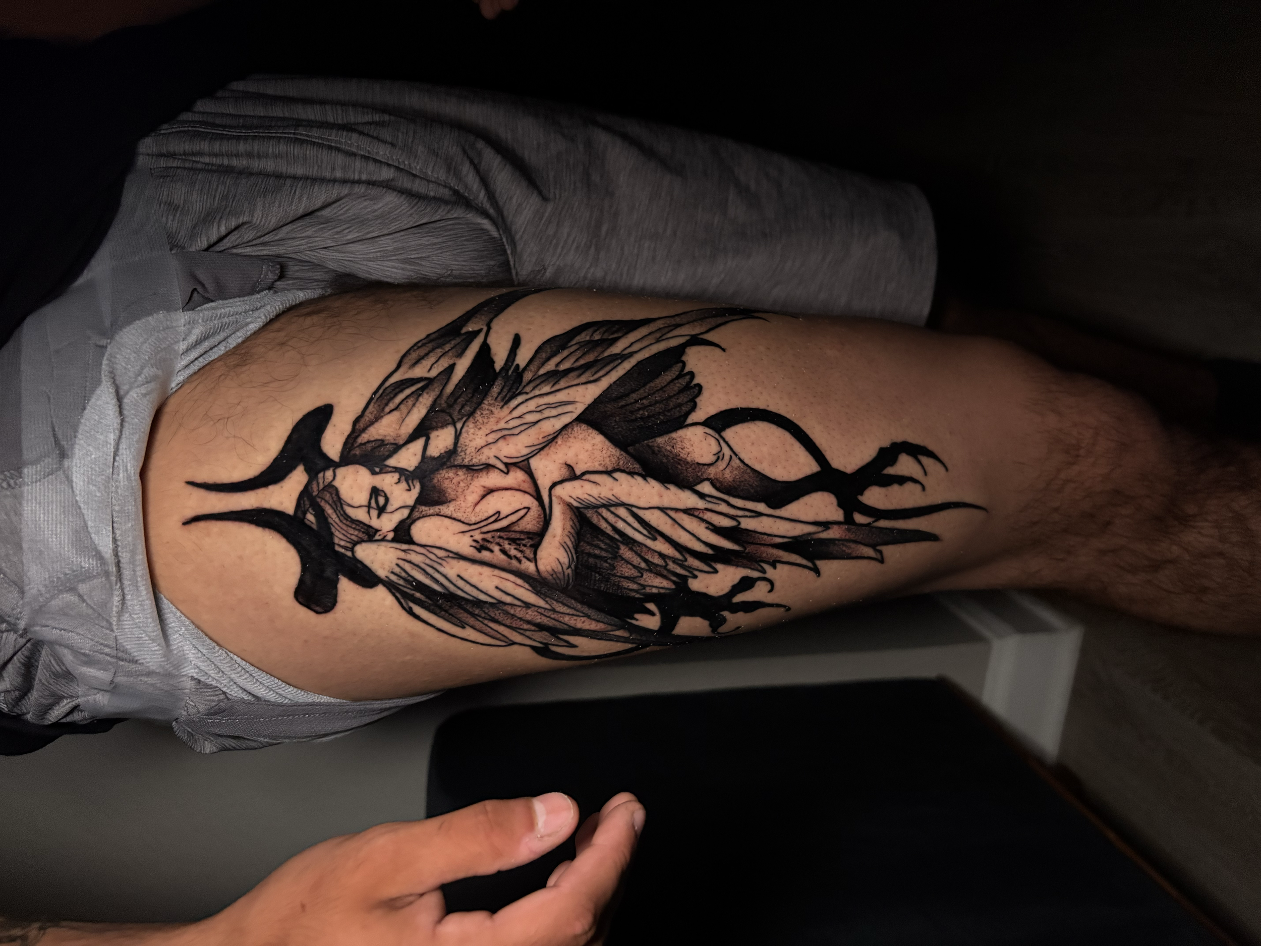 A person's upper arm with a black and gray fantasy-themed tattoo of a winged creature.