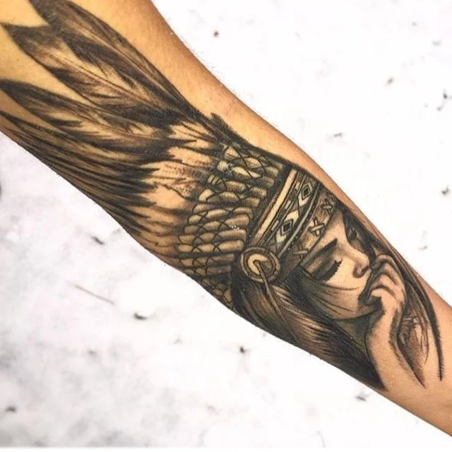 Black and gray tattoo of a Native American woman wearing a feather headdress, with the woman holding her finger to her lips in a shushing gesture.