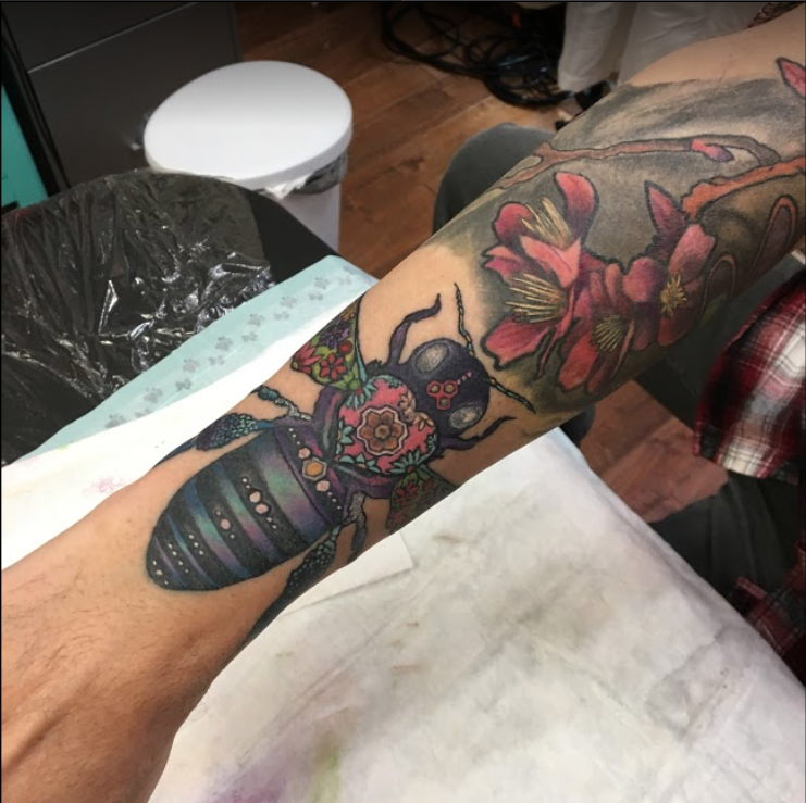 Colorful tattoo of a beetle with floral and decorative patterns on a person's arm.