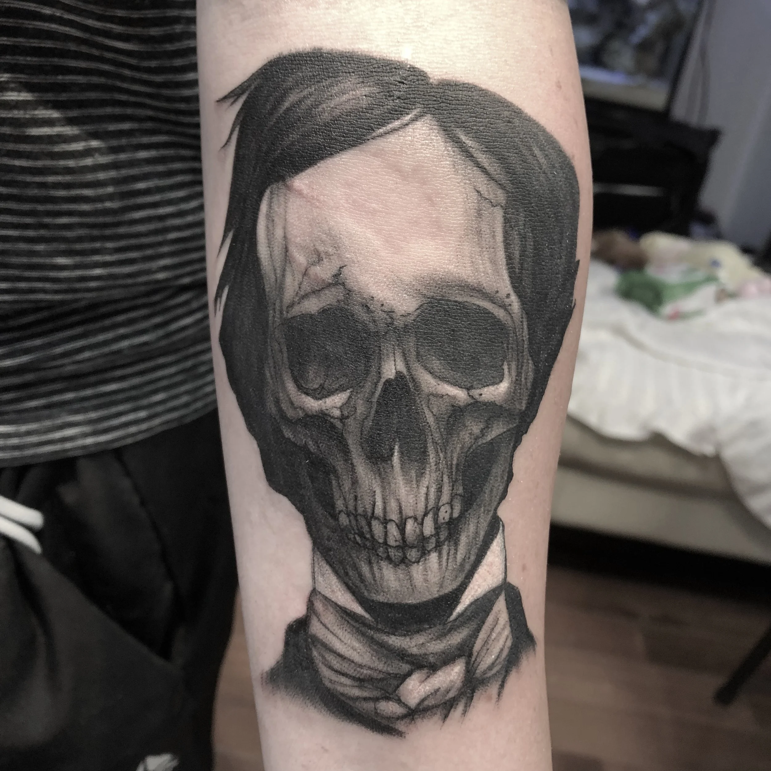 Black and gray tattoo of a human skull with a woman’s hair and a scarf around the neck.