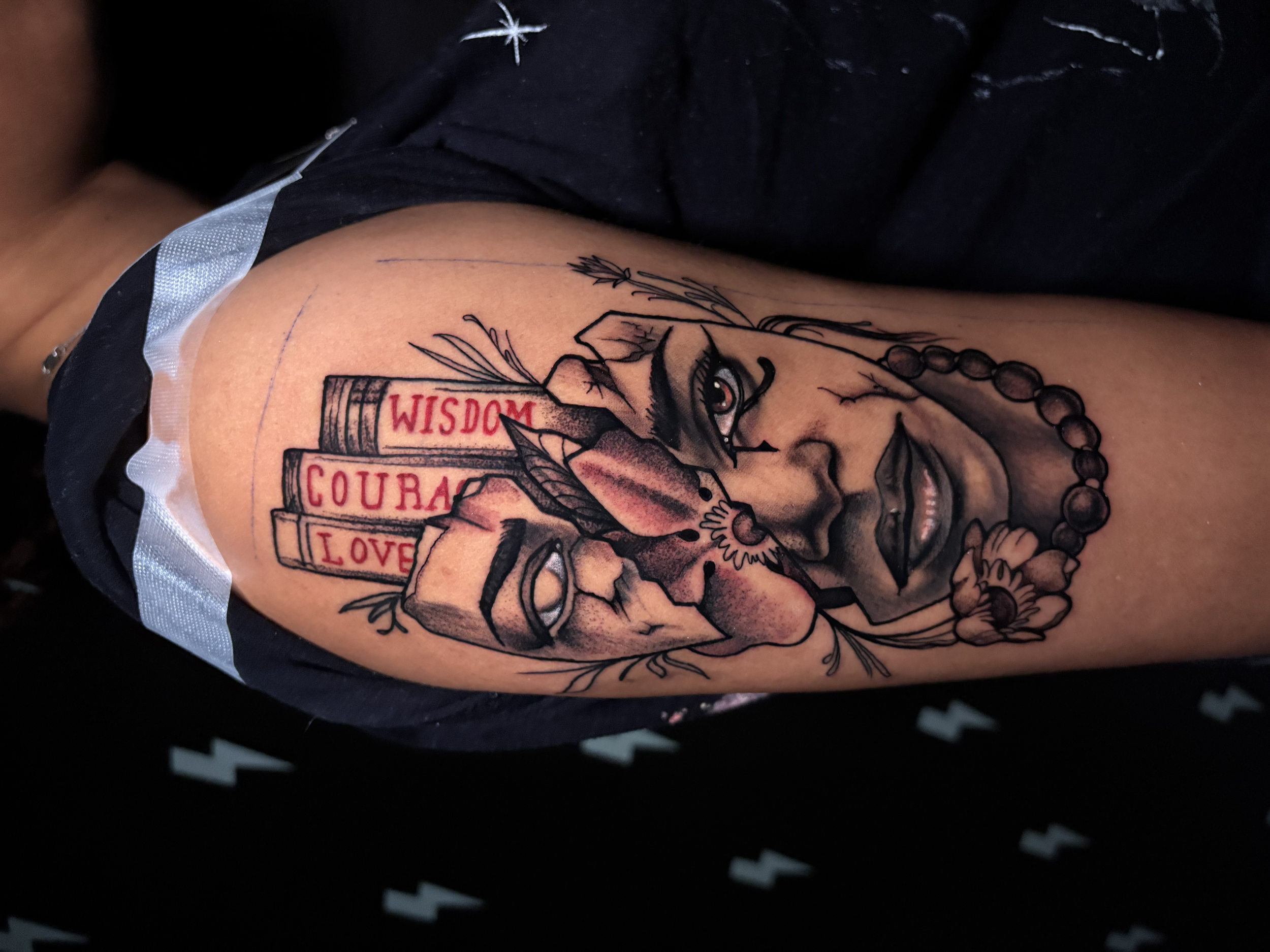 A colorful tattoo on a person's arm depicting a hand holding a vial labeled "WISDOM," with other words including "COURAGE" and "LOVE" written on the vial, and surrounded by flowers and decorative elements.