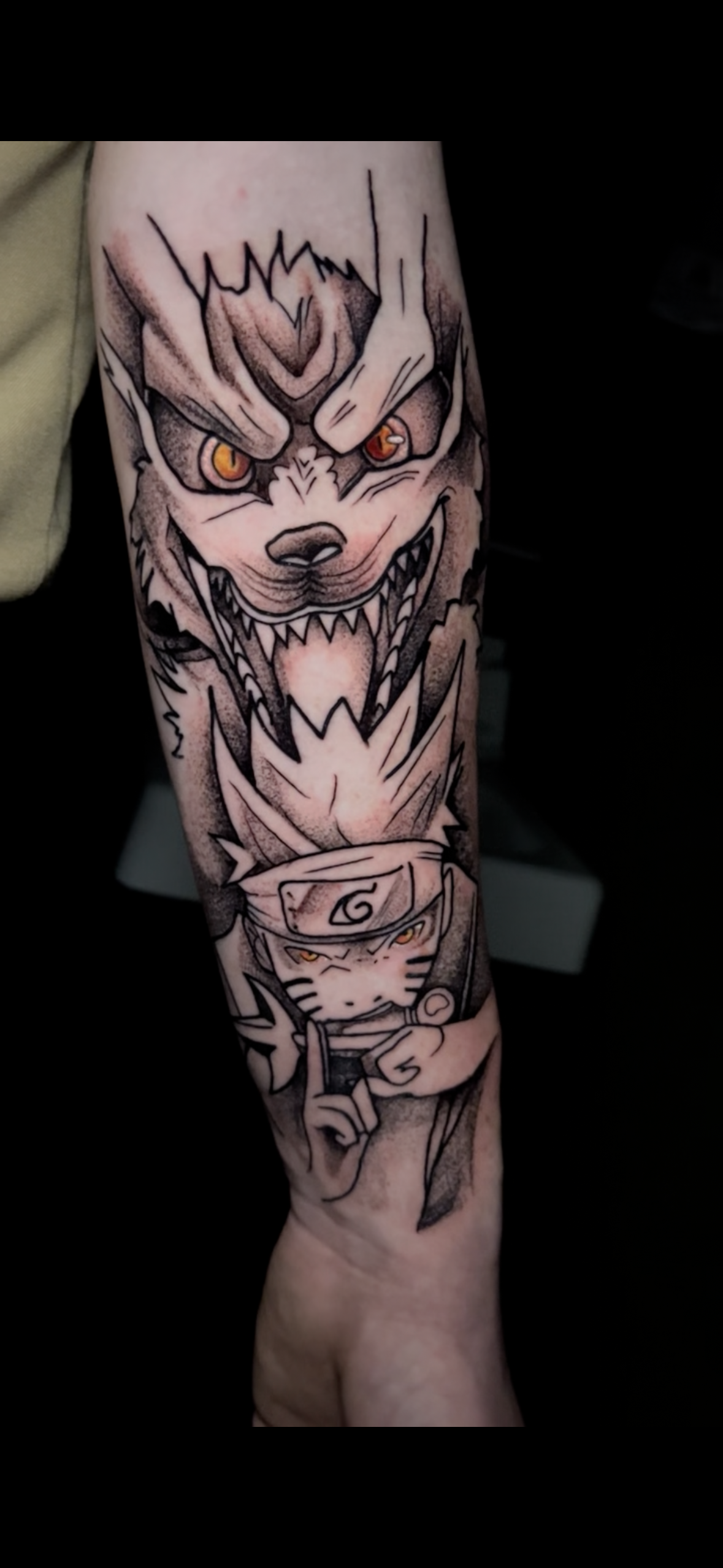 Tattoo of a fierce, cartoon-style wolf with glowing red eyes and sharp teeth, above a smaller cartoon character with a ninja headband, also with glowing eyes, holding a scroll.