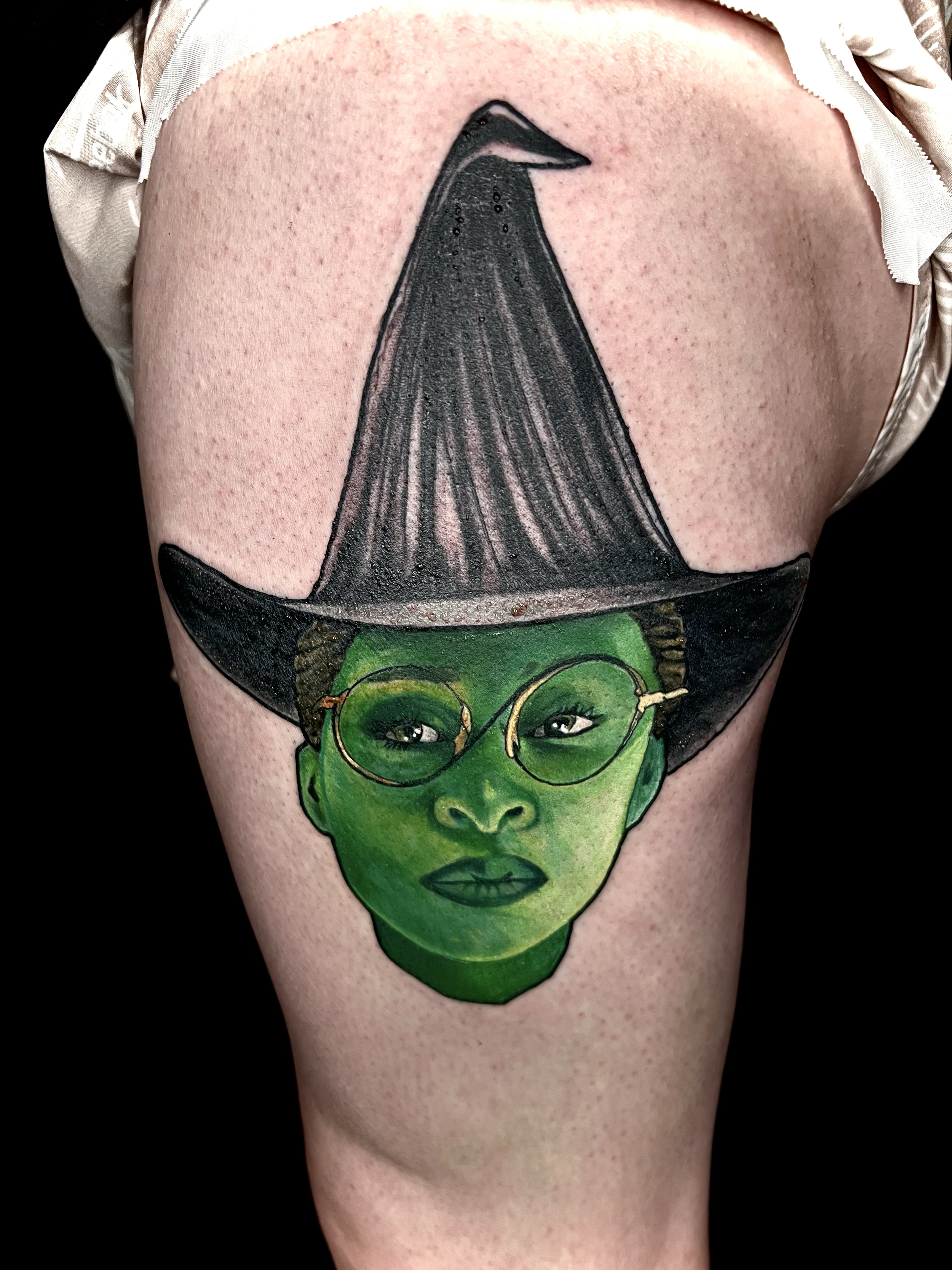 Elphaba inspired Wicked tattoo featuring a vivid green portrait, black witch hat, and bold illustrative color work by Salvador Vargas III, serving Bluffton SC, Savannah GA, and Charleston SC.