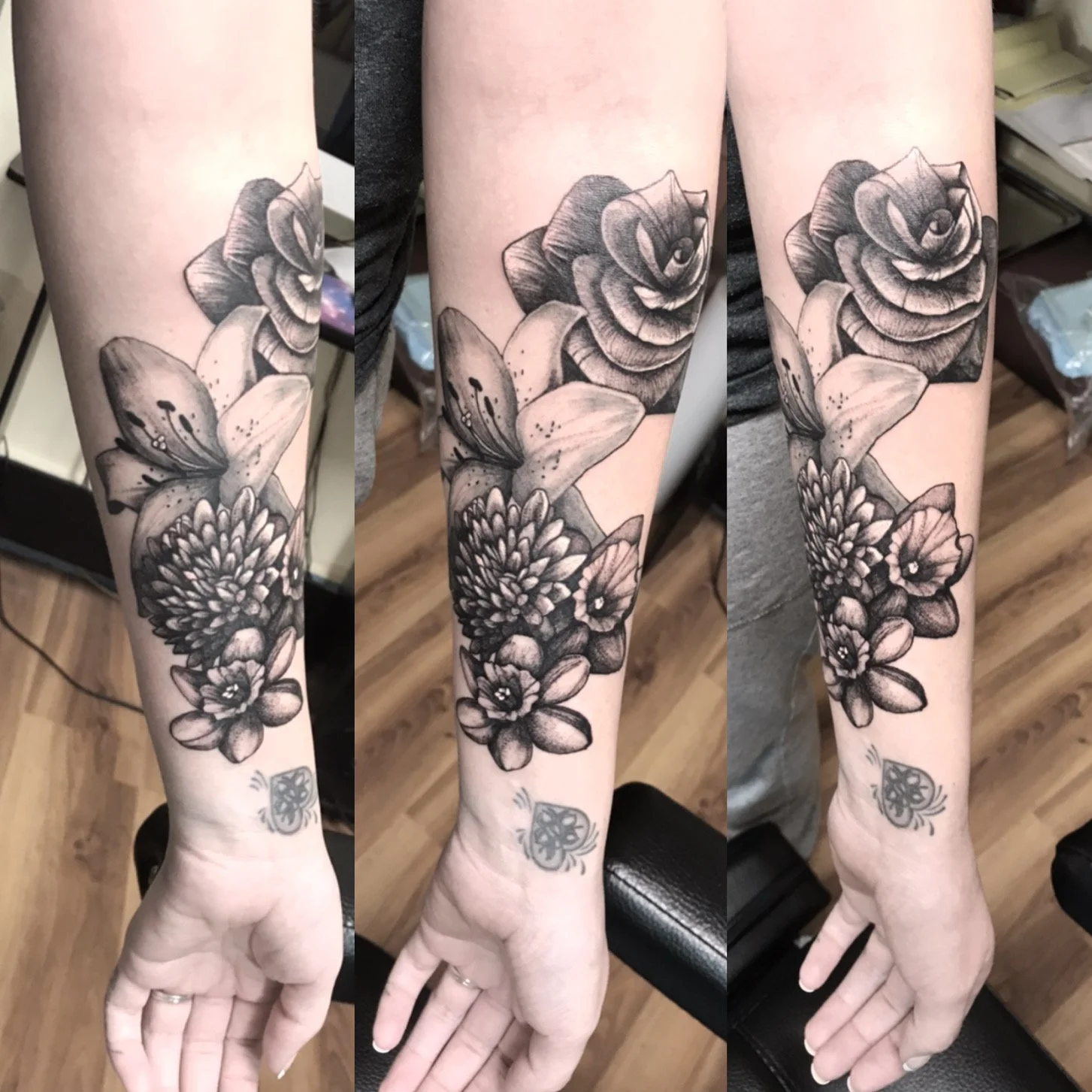 Black and gray floral tattoo sleeve on person's forearm, featuring various flowers including a large open rose, lilies, and smaller blossoms.