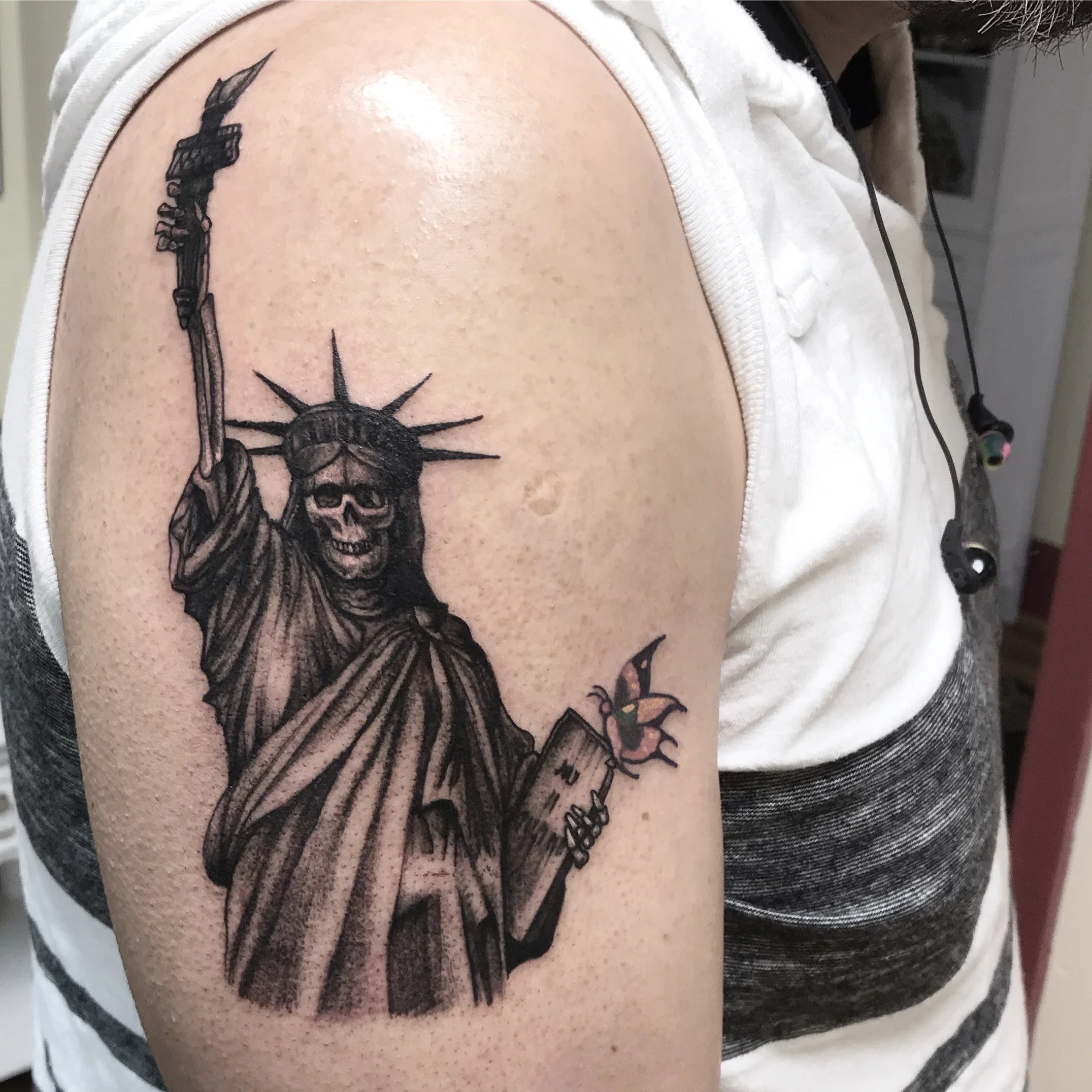 Tattoo of the Statue of Liberty with a skull face, holding a book and a torch.