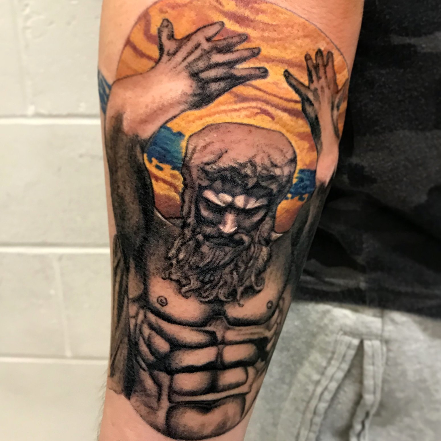 Tattoo of a bearded man with a halo, hands raised, with Christian symbolism on the arm.