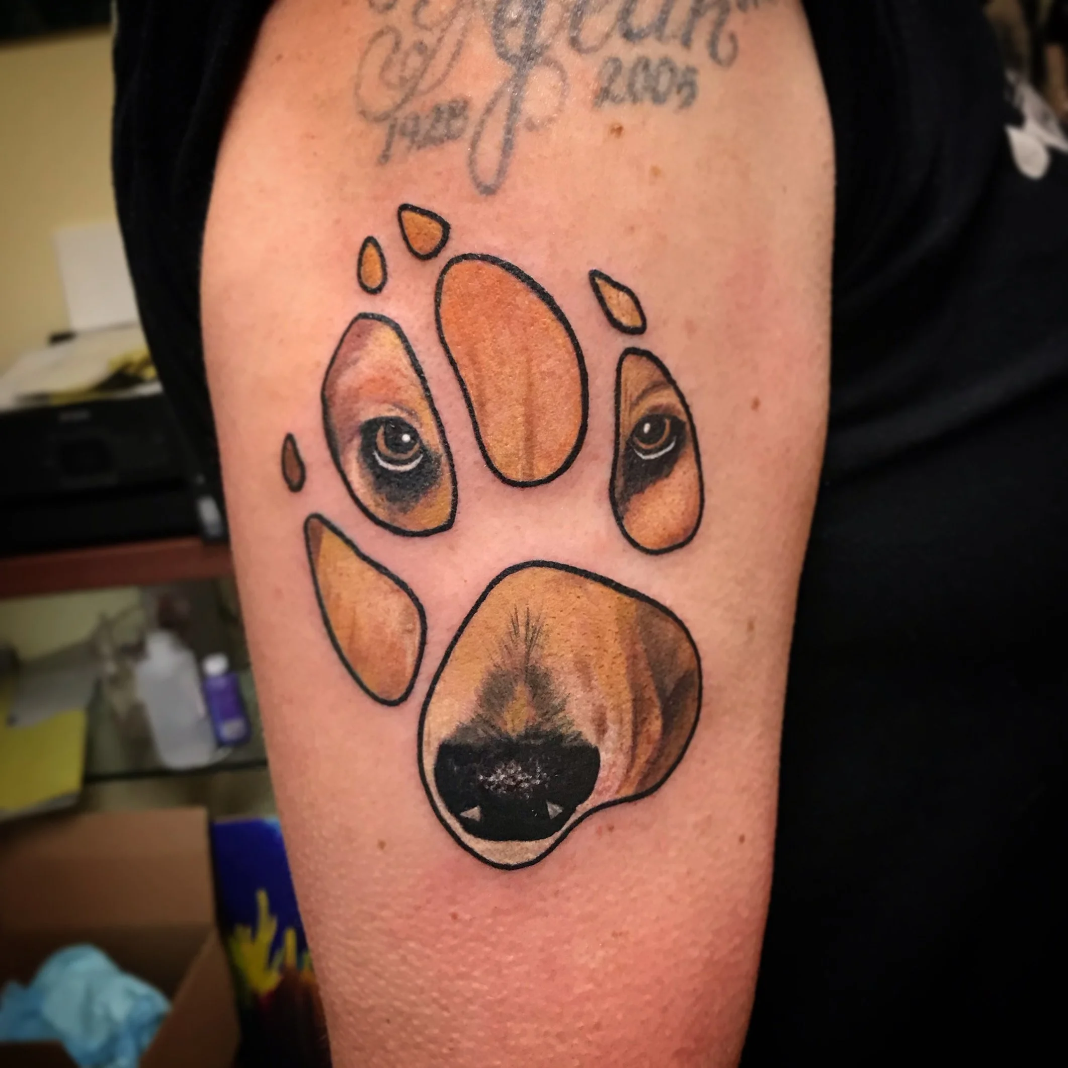 Tattoo of a dog paw print with realistic eyes and nose details on a person's upper arm.