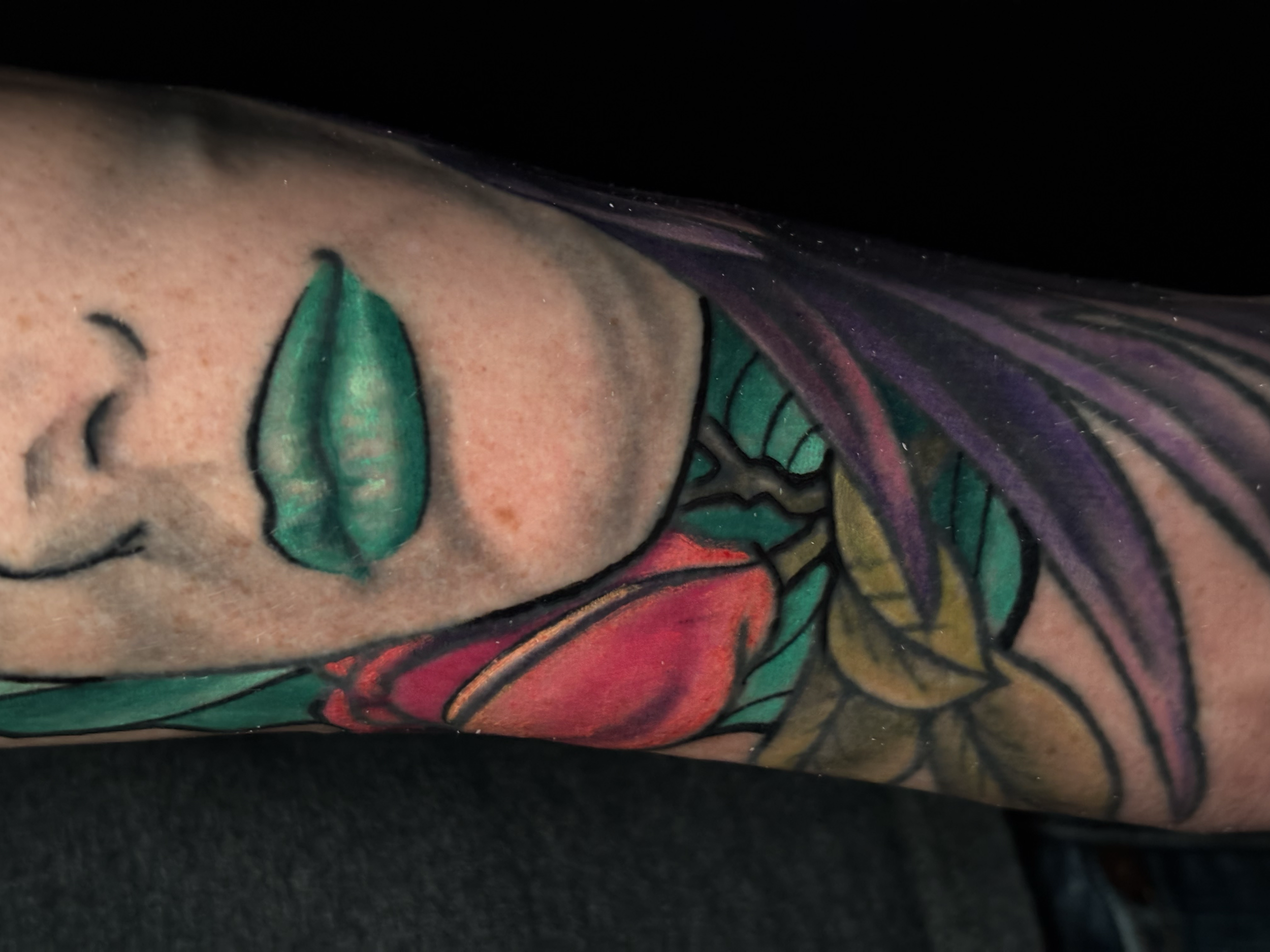 Close-up of a colorful tattoo of a woman's face with purple hair and green leaves on skin.