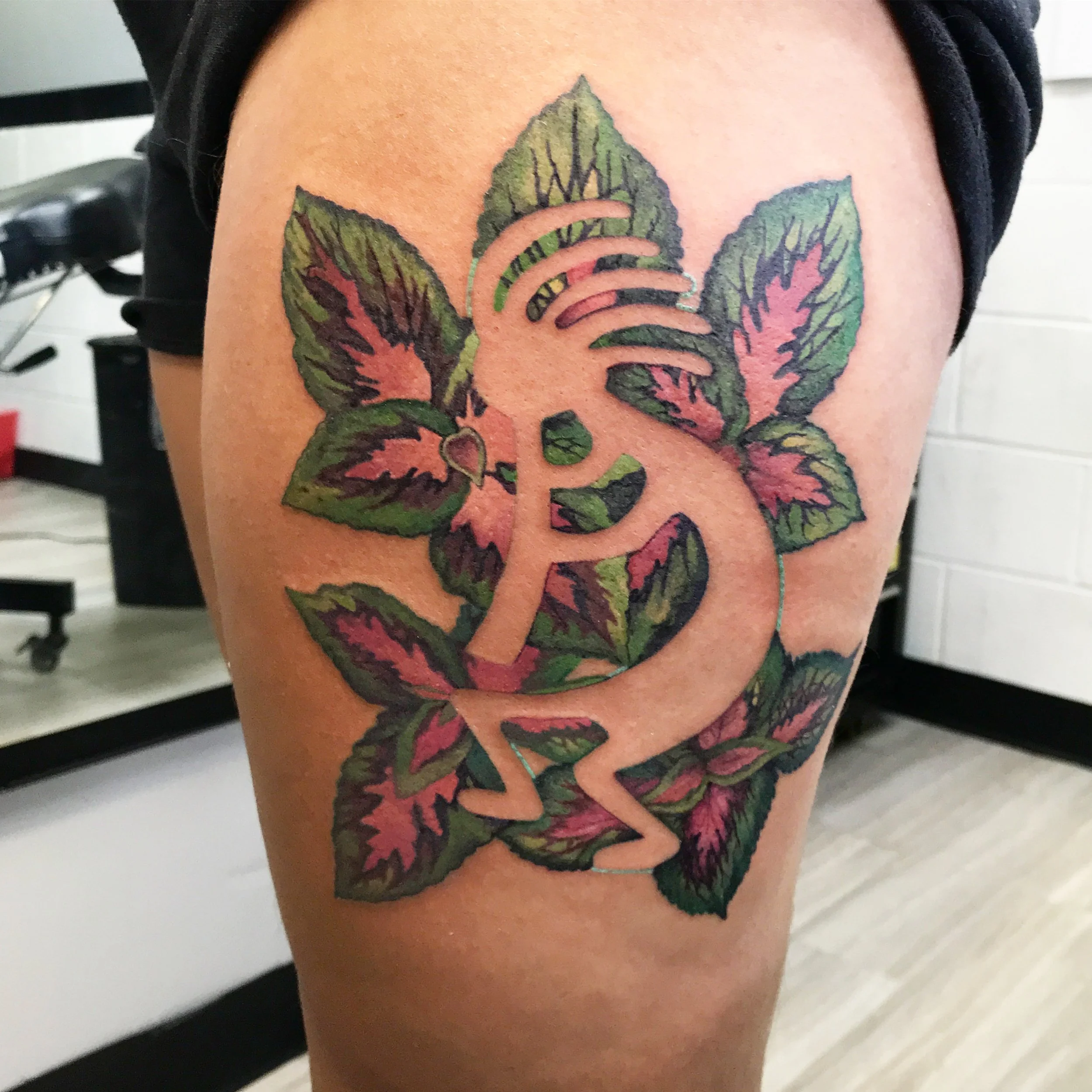 Tattoo of a DNA helix with leaf designs in green, pink, and black colors on upper thigh.