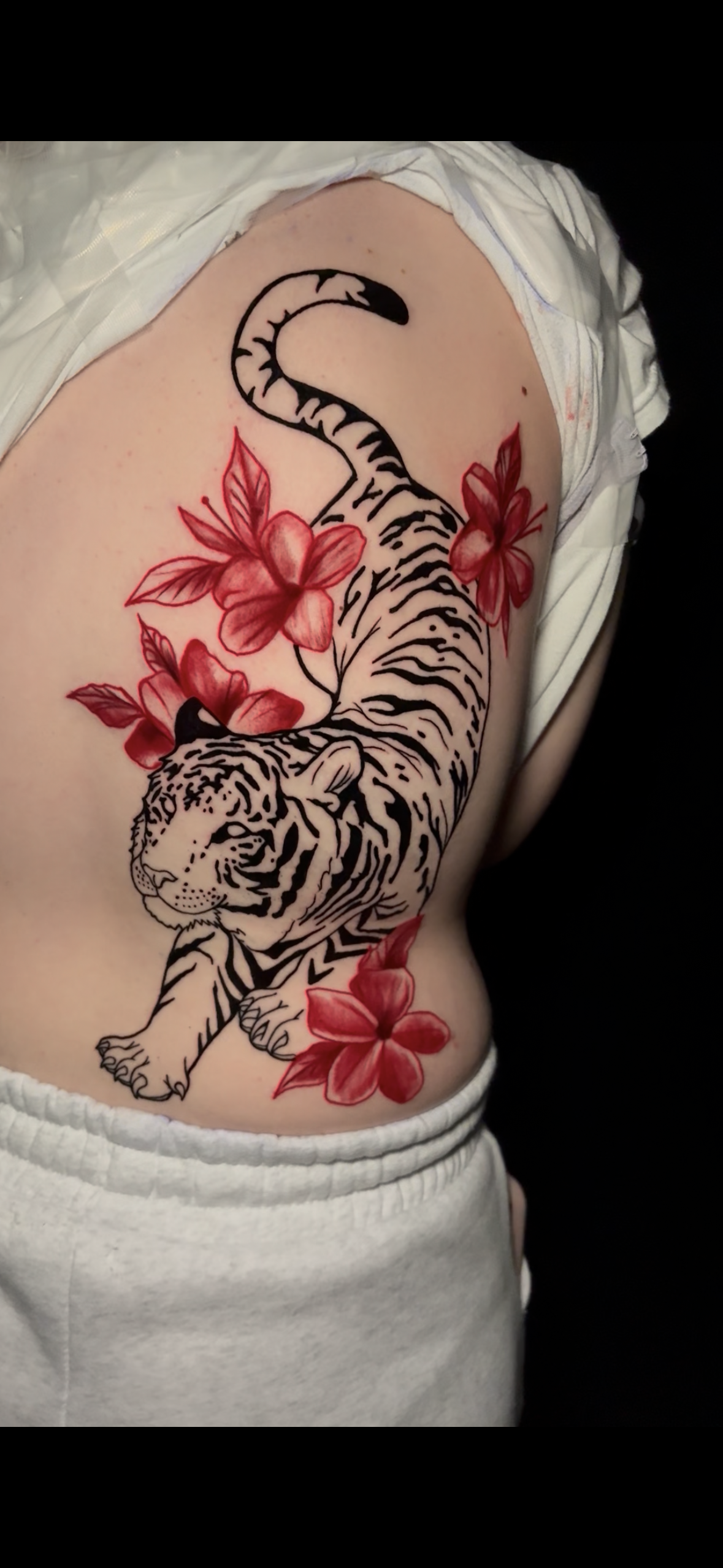 A tattoo of a tiger with black and white stripes surrounded by red flowers on the person's upper arm and shoulder.