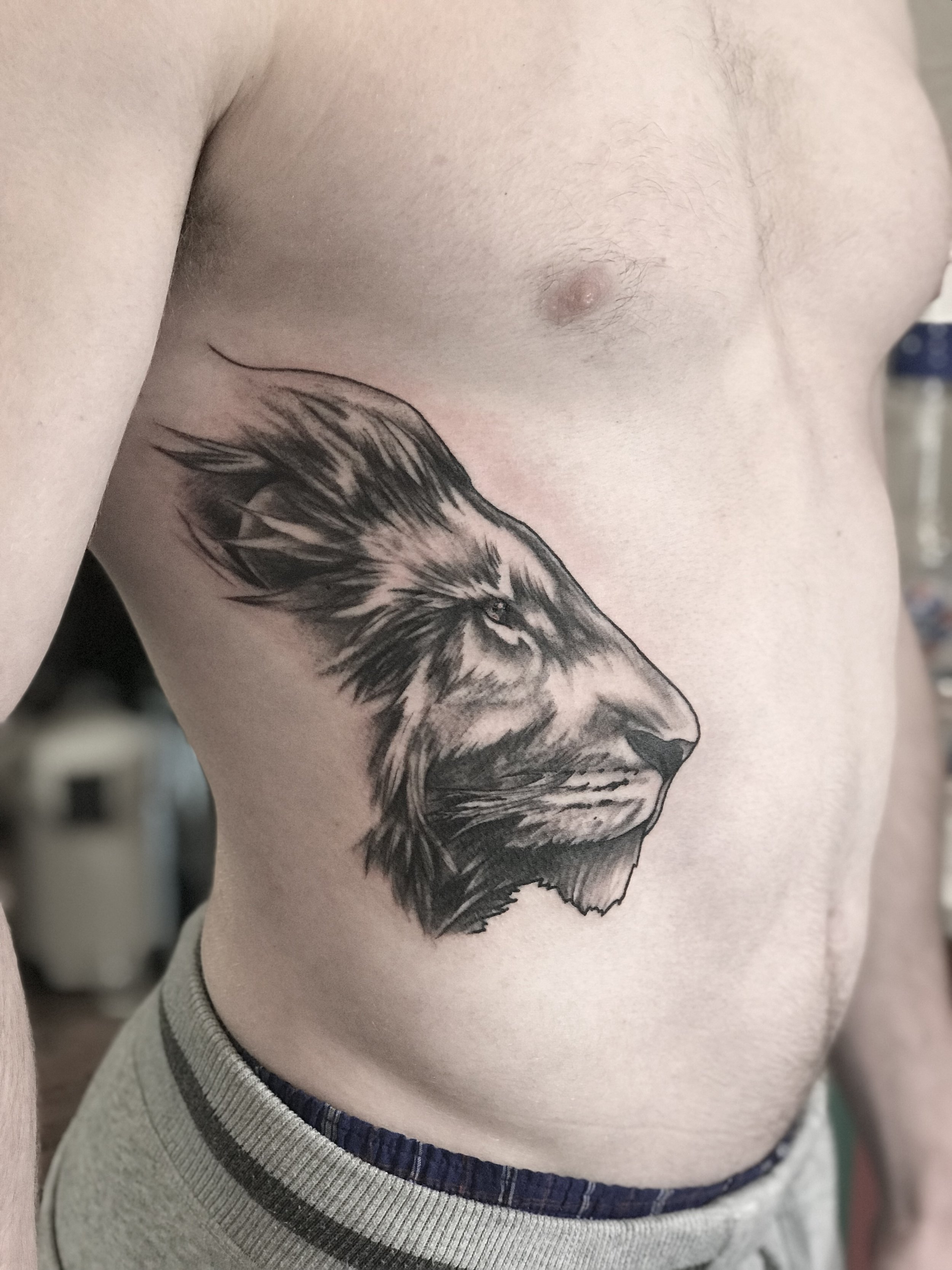 Tattoo of a lion's head on a person's left side of chest in black and gray.