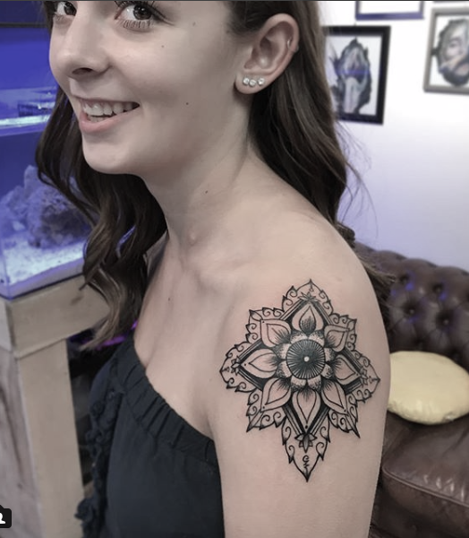Young woman smiling, showing a large black and gray fine line  floral mandala tattoo on her upper arm and shoulder. 