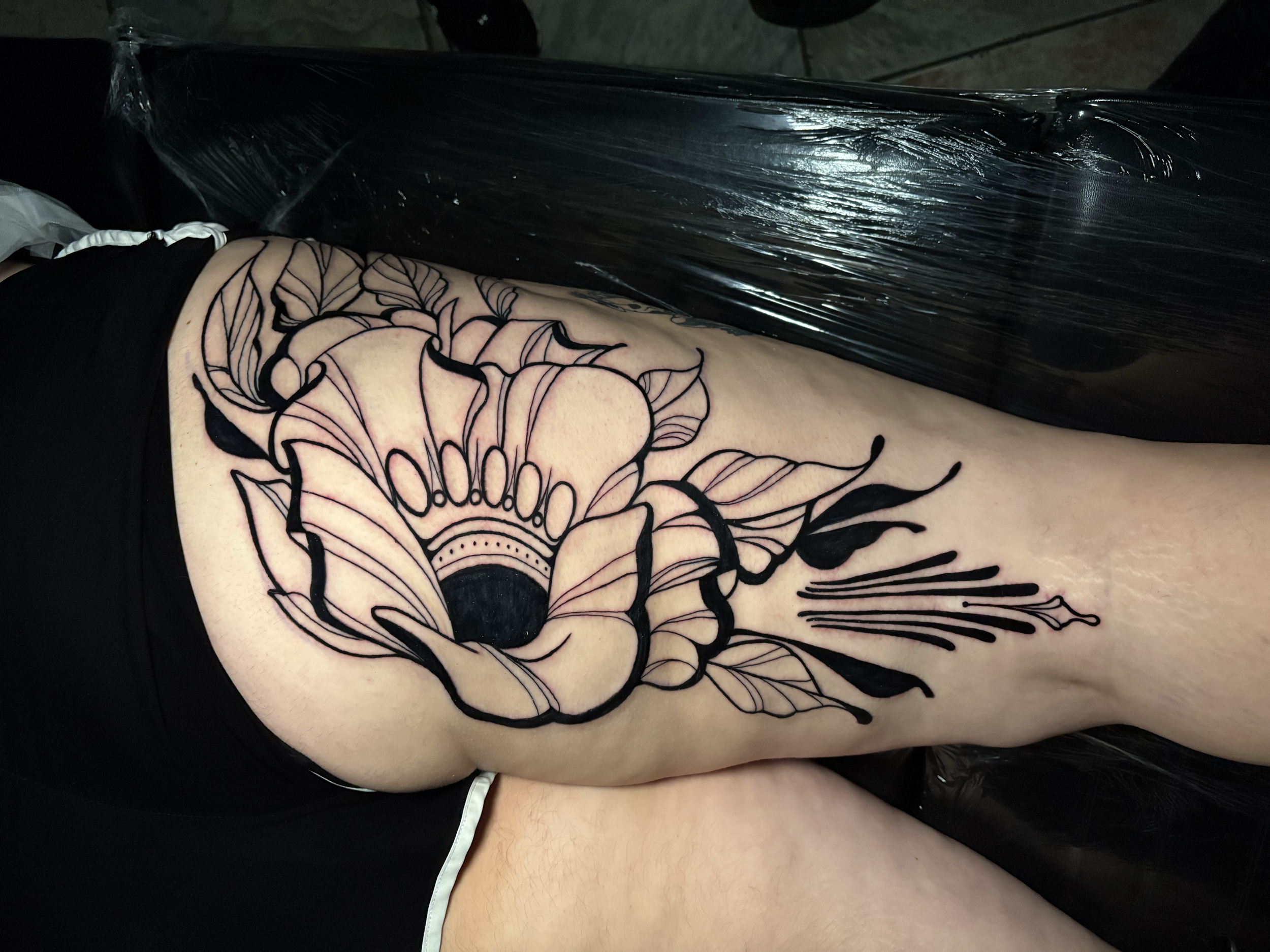 A person with a floral tattoo on their side, lying on a chair, with plastic wrap covering their torso.