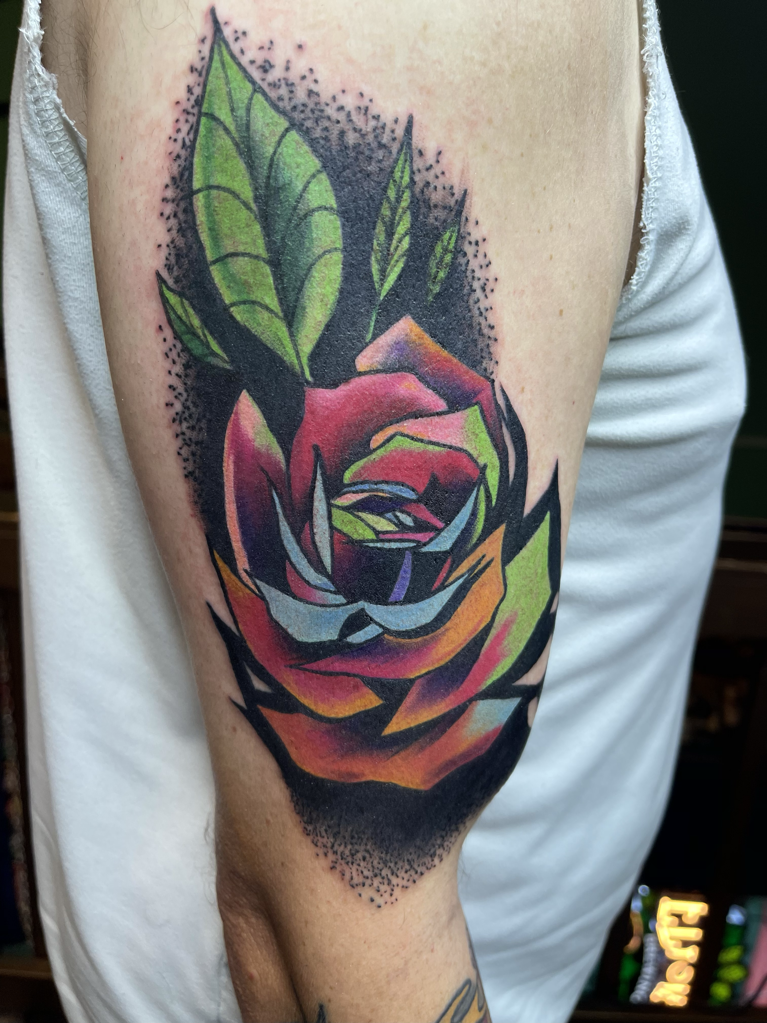 Color tattoo of a rose with leaves on person's upper arm.