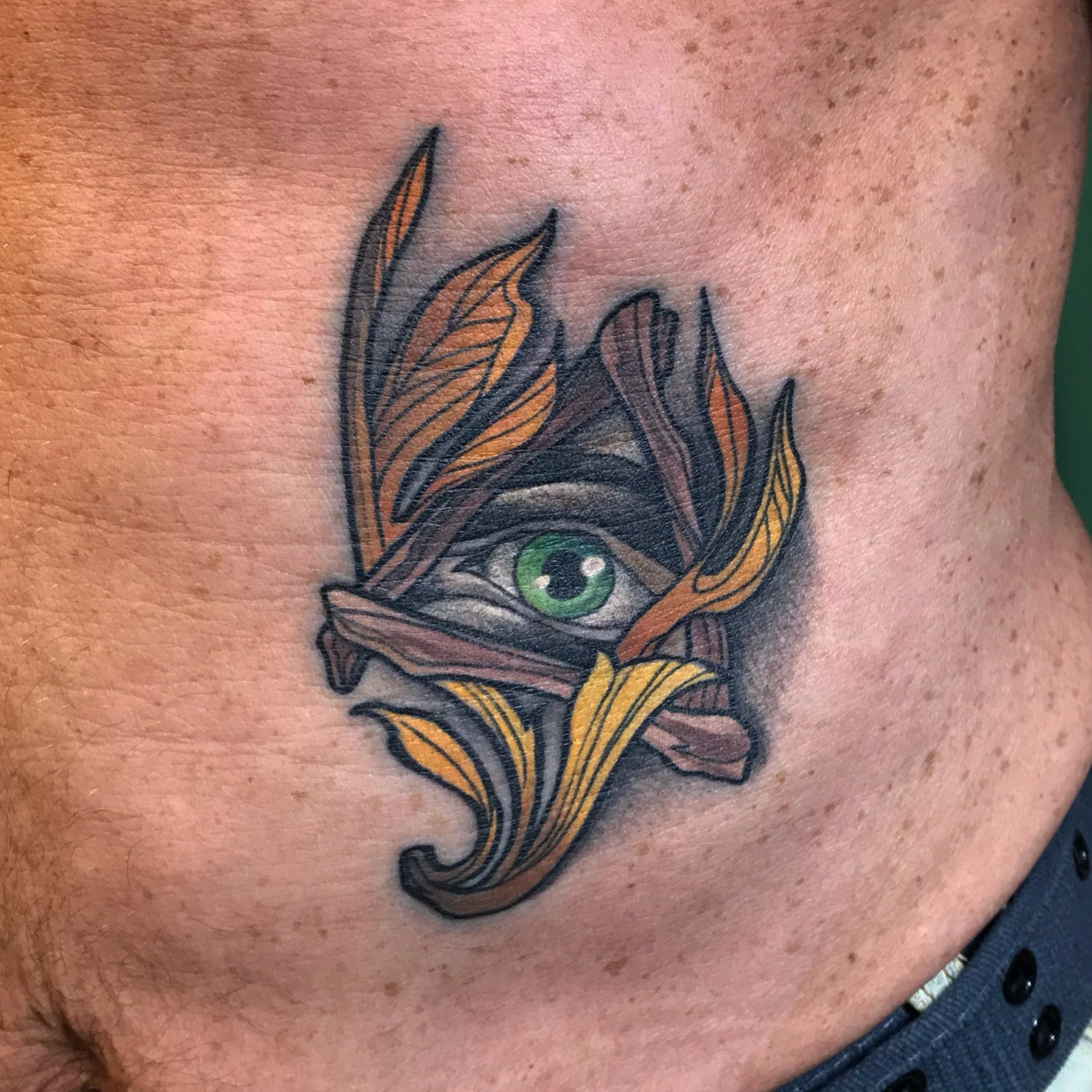 Neo traditional Tattoo of a green eye surrounded by and intertwined with orange and brown leaves on the person's skin.