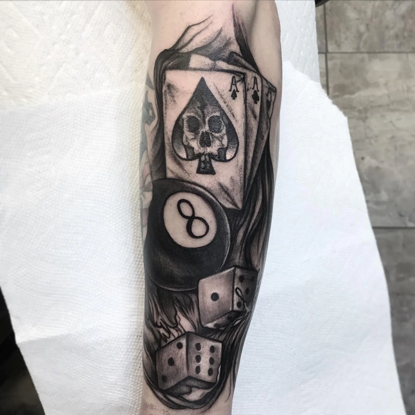 Tattoo of playing cards with a skull in the spade suit, a billiard ball with the number 8, and a pair of dice.