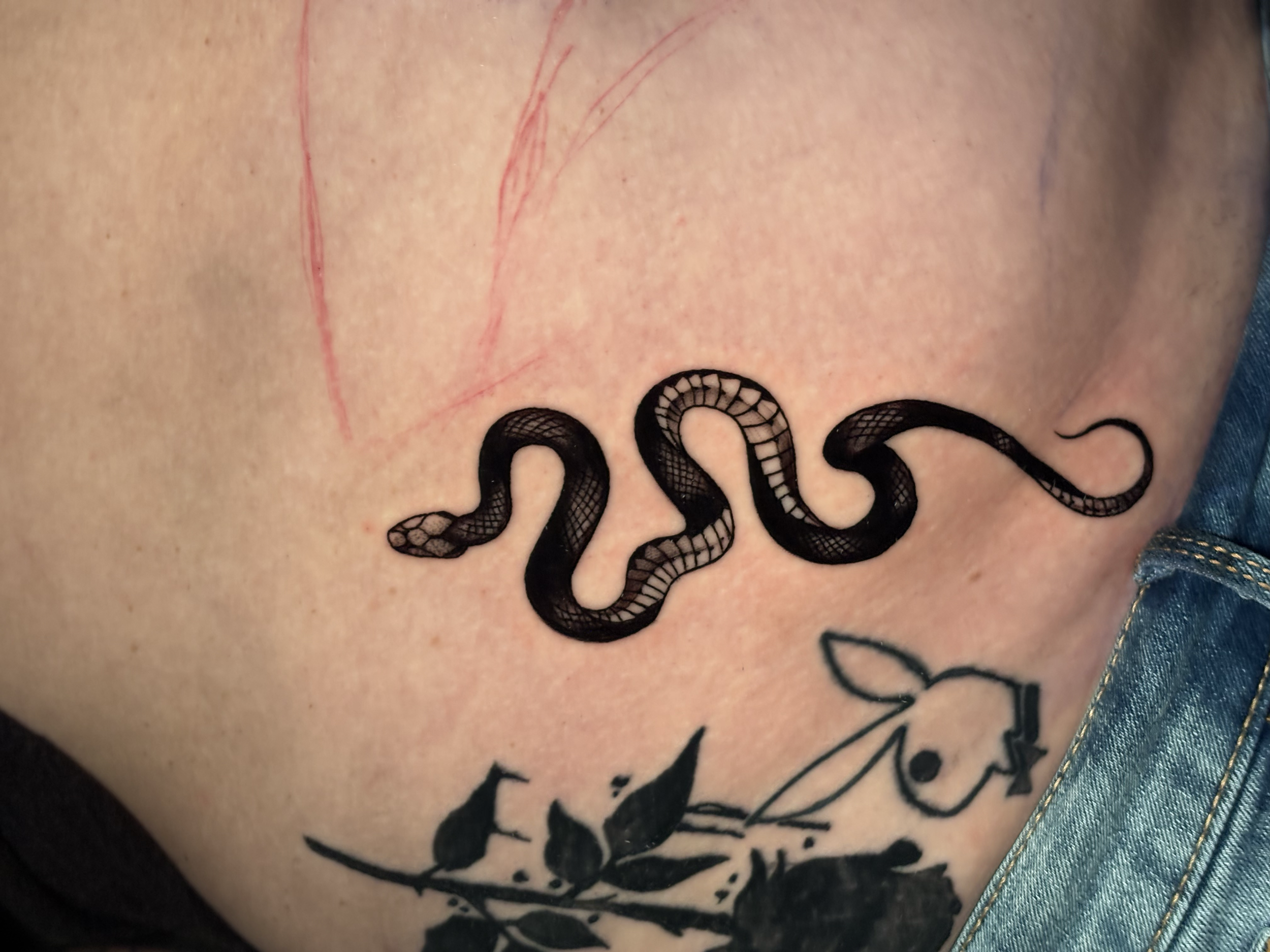 Close-up of a person's skin with red scratches and black ink tattooed text reading '2023' and some other partially visible letters near the bottom.