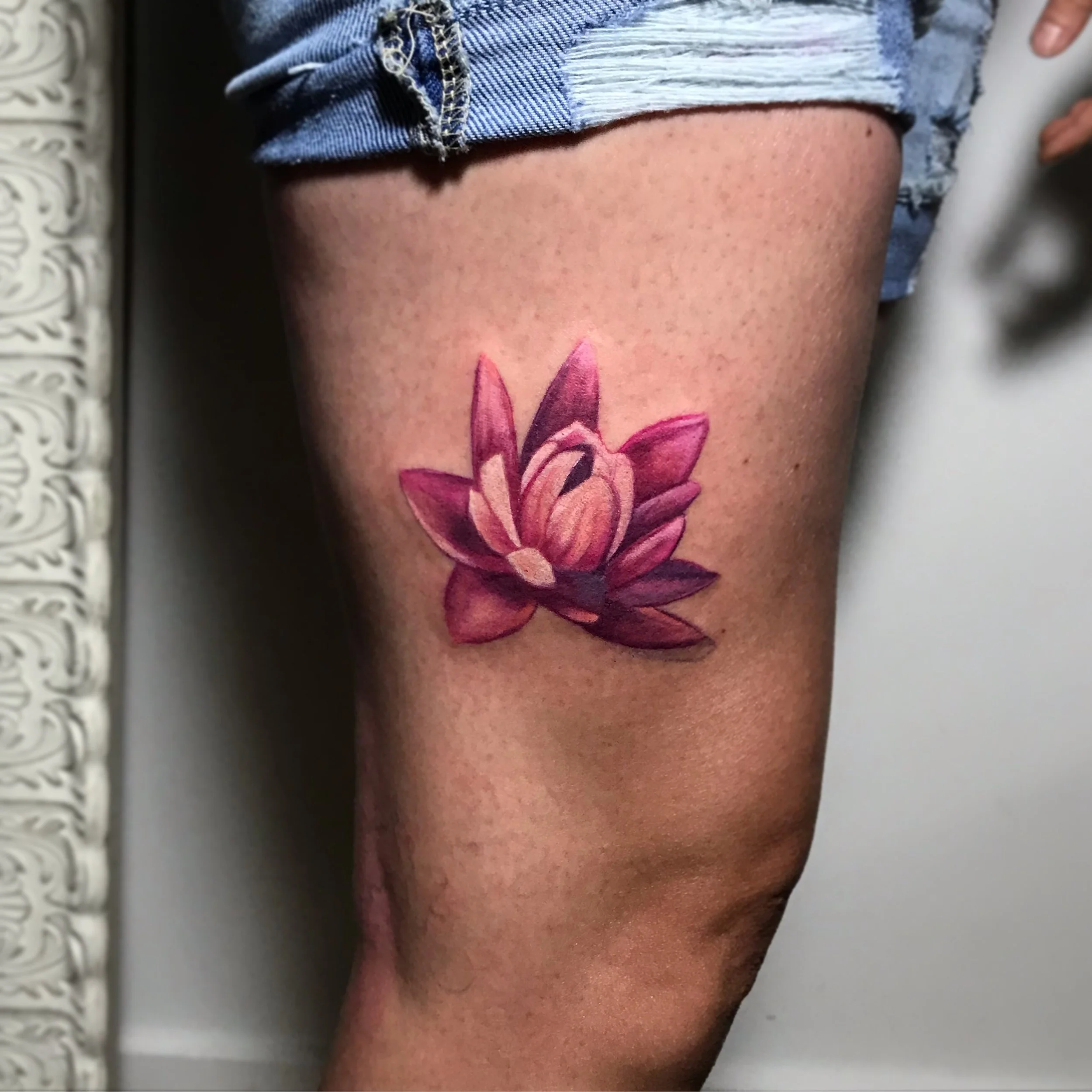 A colorful pink and purple lotus flower tattoo on a person's thigh.