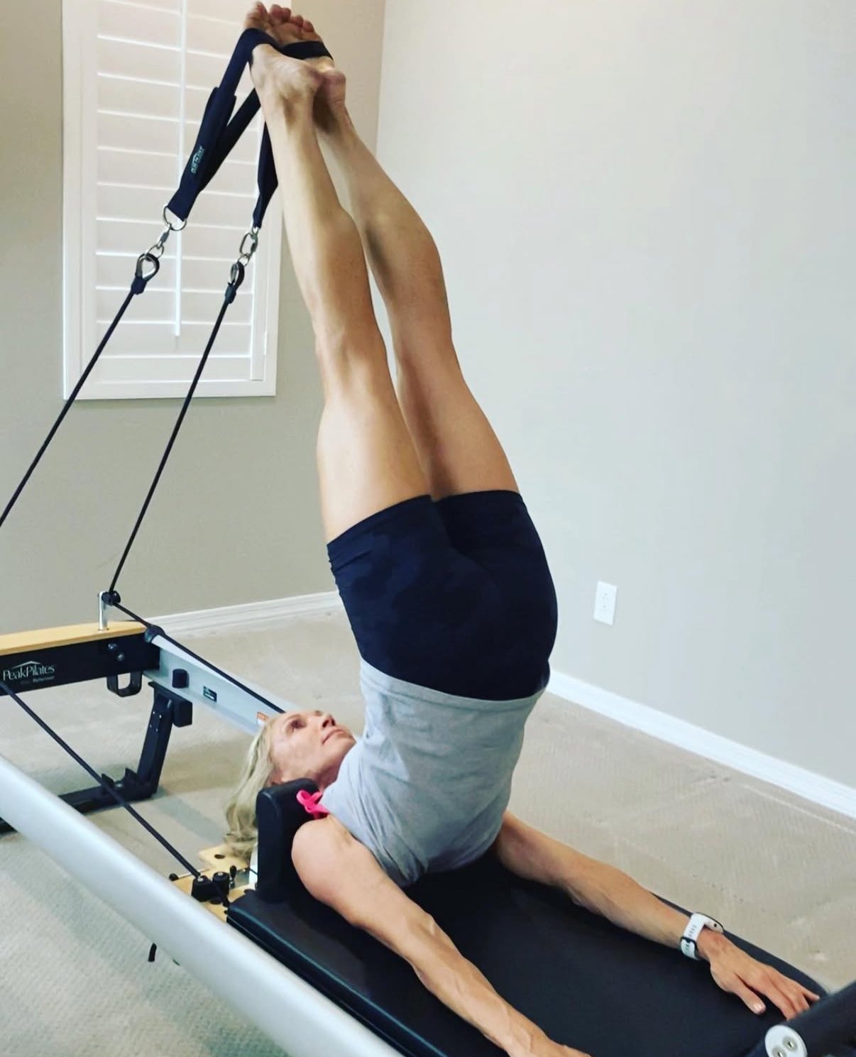 A woman exercising on a Pilates Peak MVe Reformer wearing Lululemon athletic wear performing the exercise Short Spine with her feet in the straps.