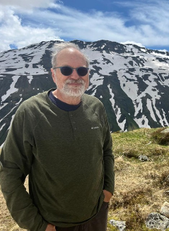An man with white hair and beard with mountains in the background
