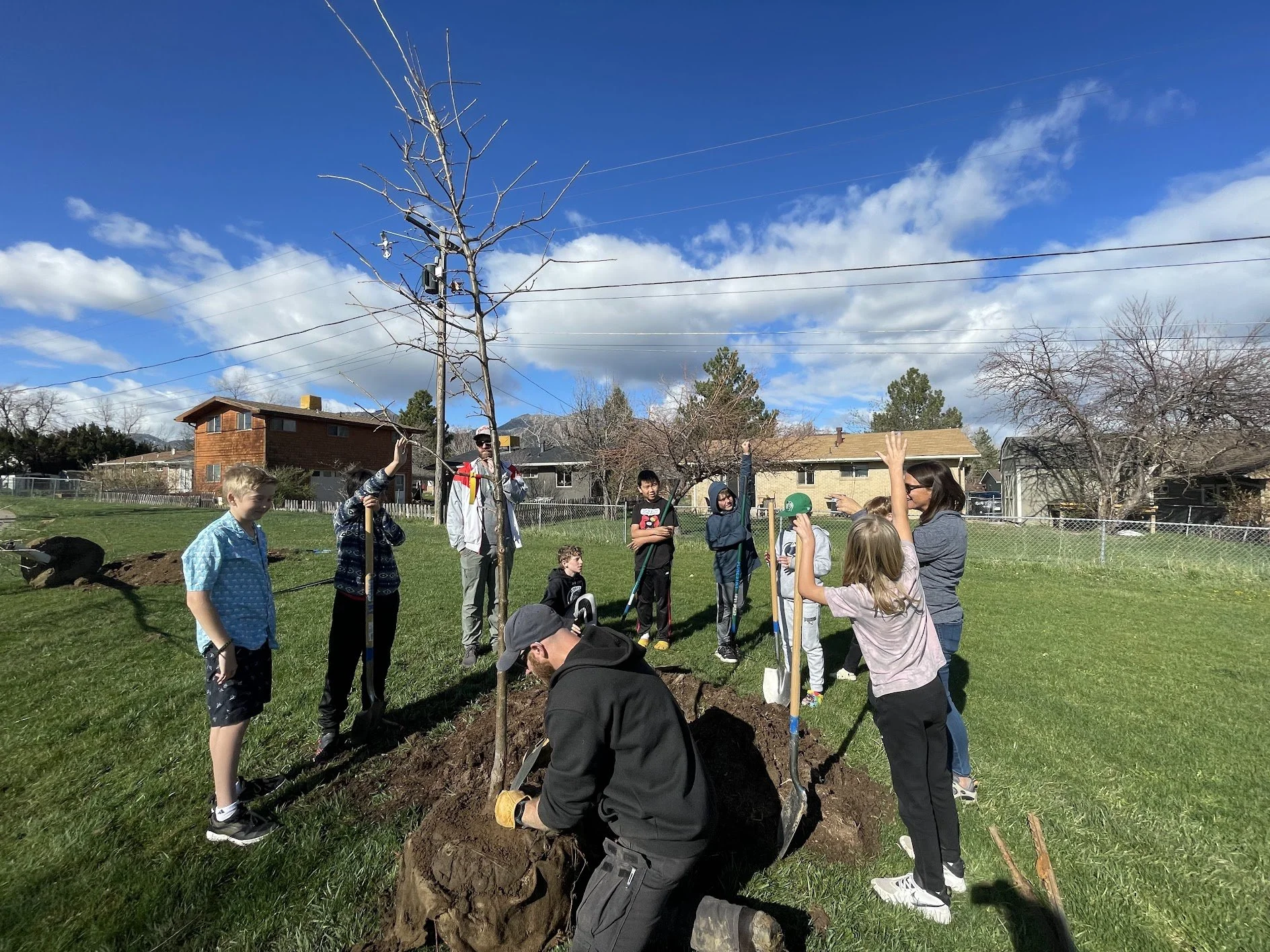 Several students gather around a tree outside and watch an instructor tend to it.