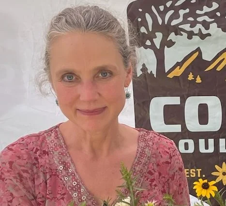 An older woman standing in front a banner with the Cool Boulder logo on it.