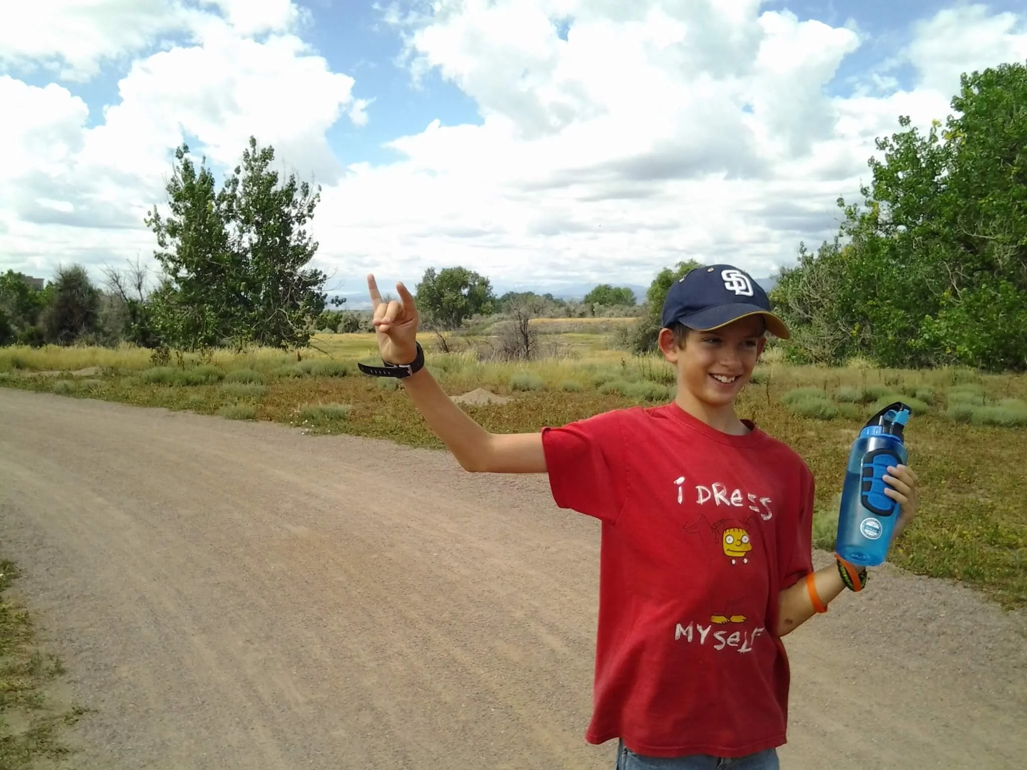 Boy in baseball cap and red shirt smiling on a nature trail.