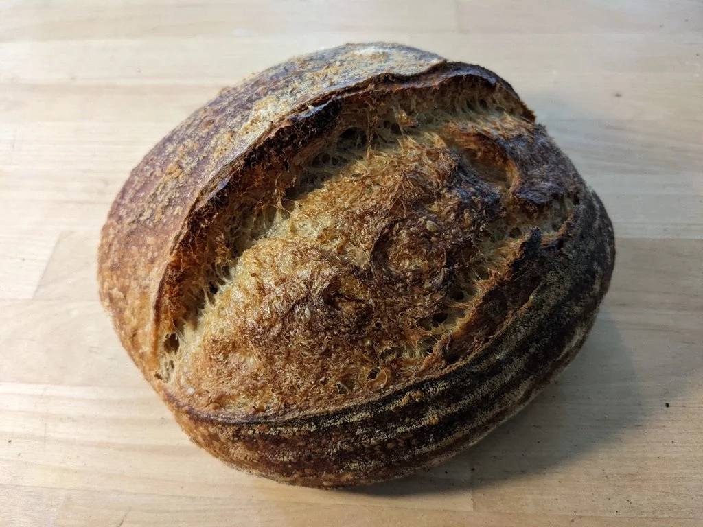 A loaf of rustic, artisan sourdough bread with a dark, crusty exterior and a textured surface.