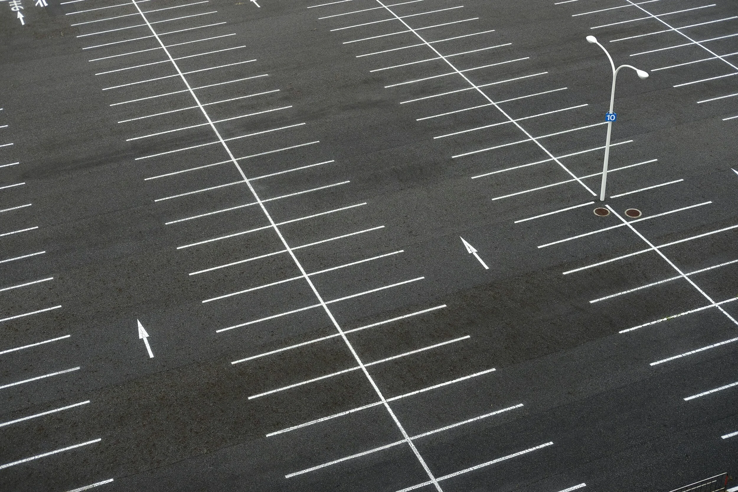 Empty parking lot with marked spaces and arrows, featuring a street lamp and number 10 sign.