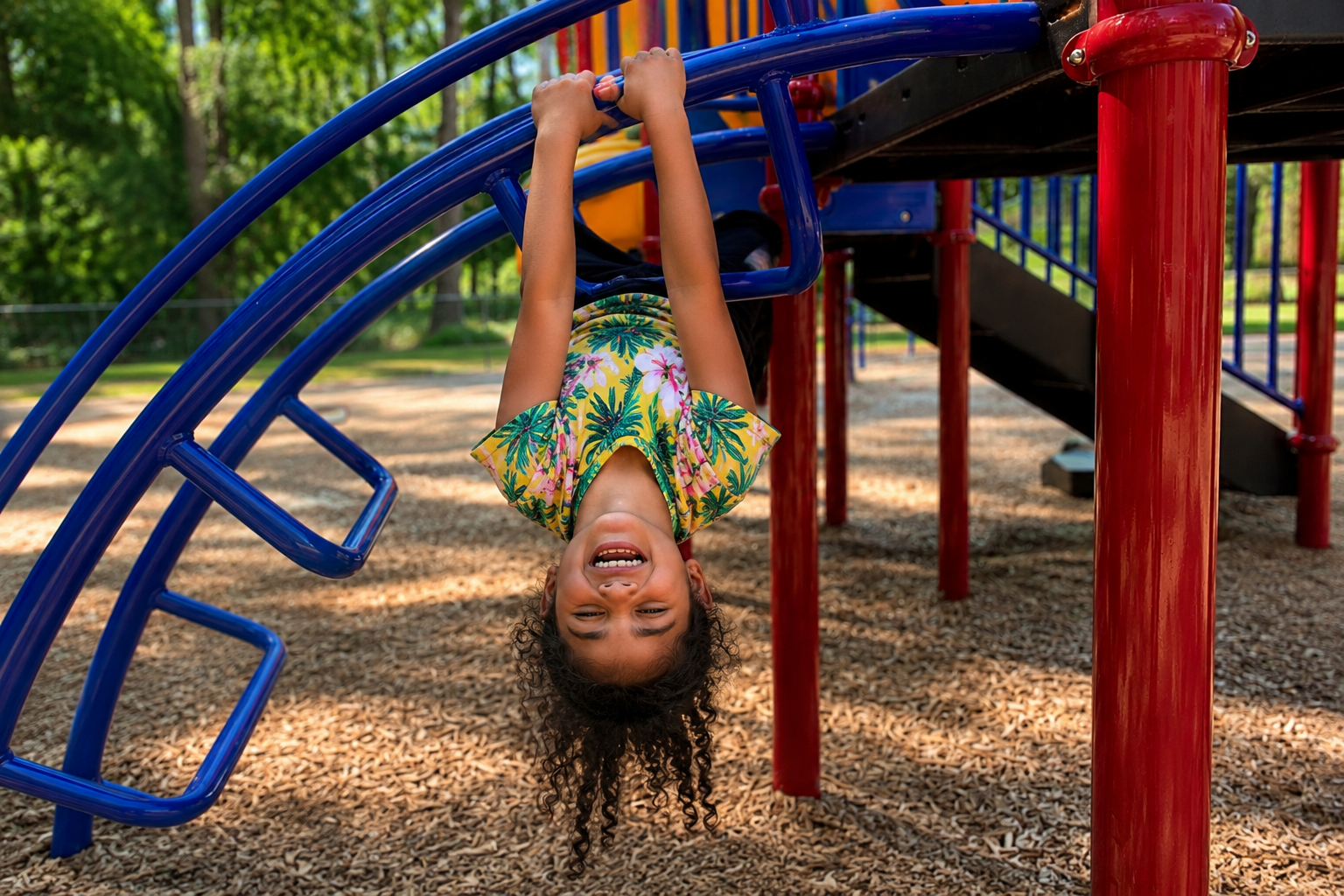 a small child hangs upside down on the playset.