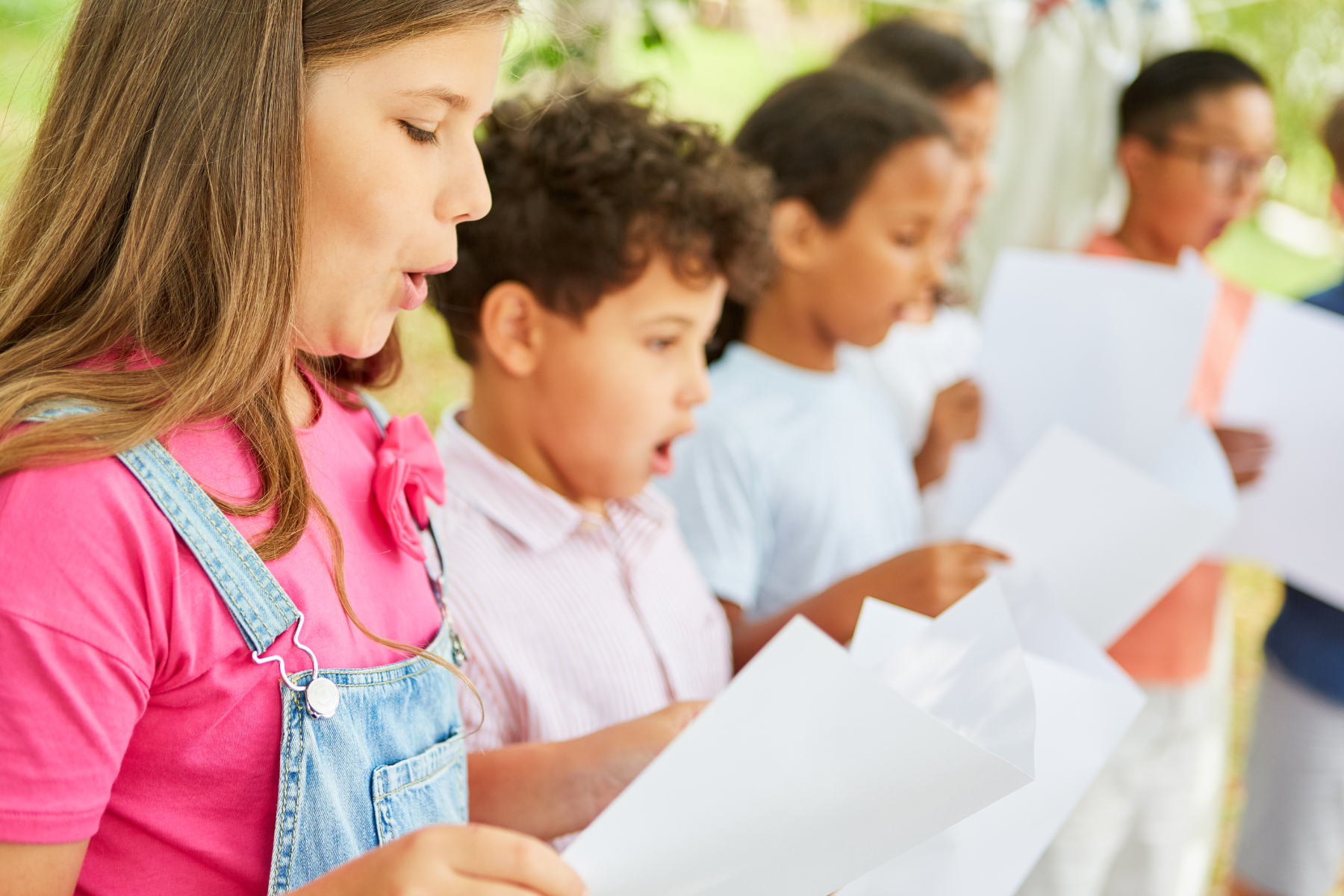 A group of children sing together with papers.