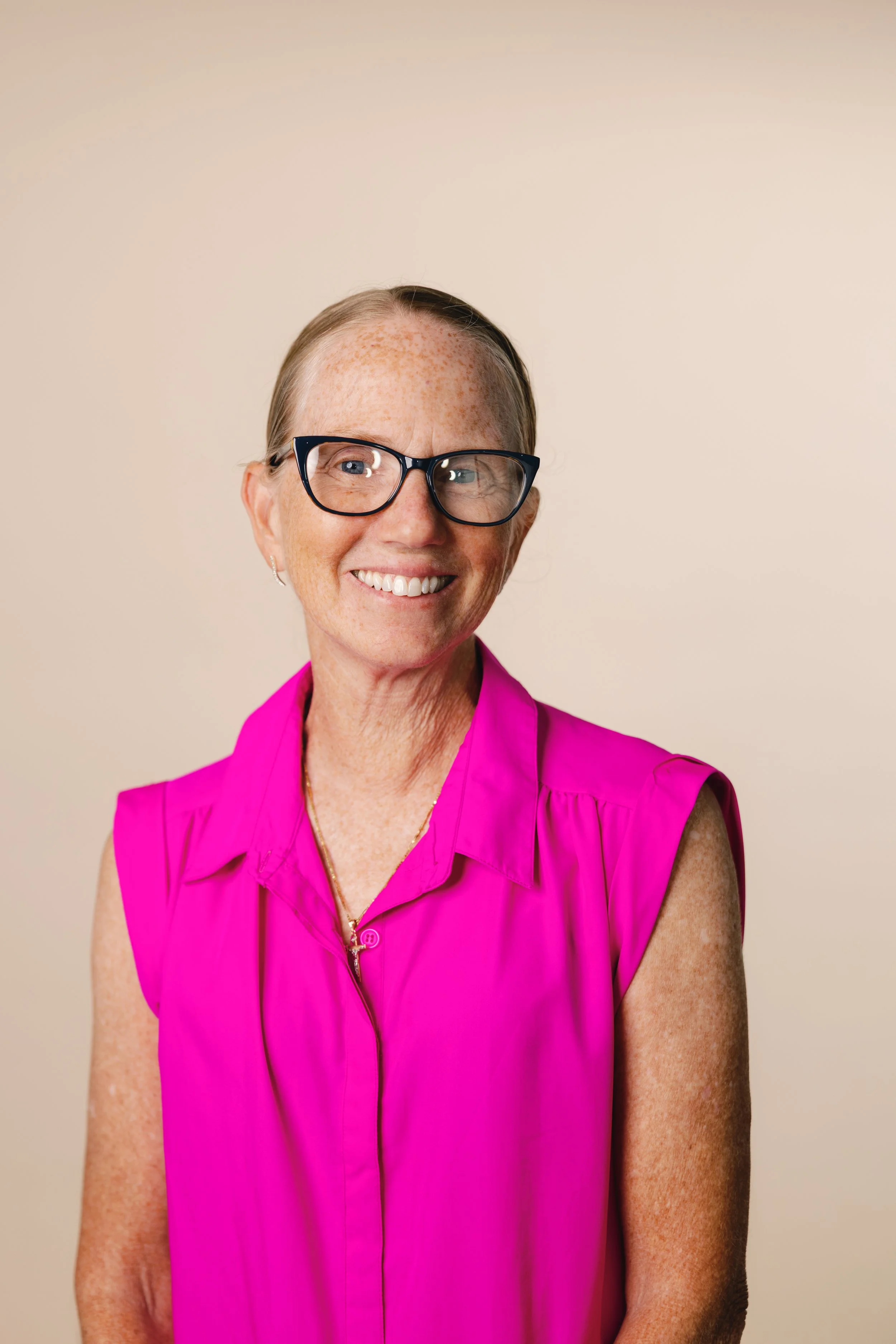 Woman wearing glasses and hat smiles at camera.