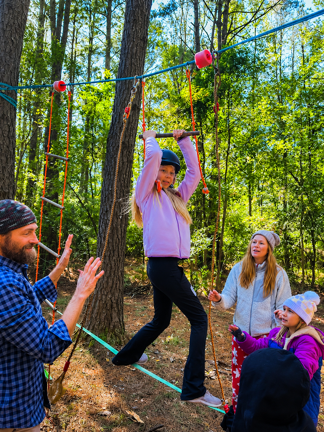 A girl walks along a slackline with the help of parent-aides.
