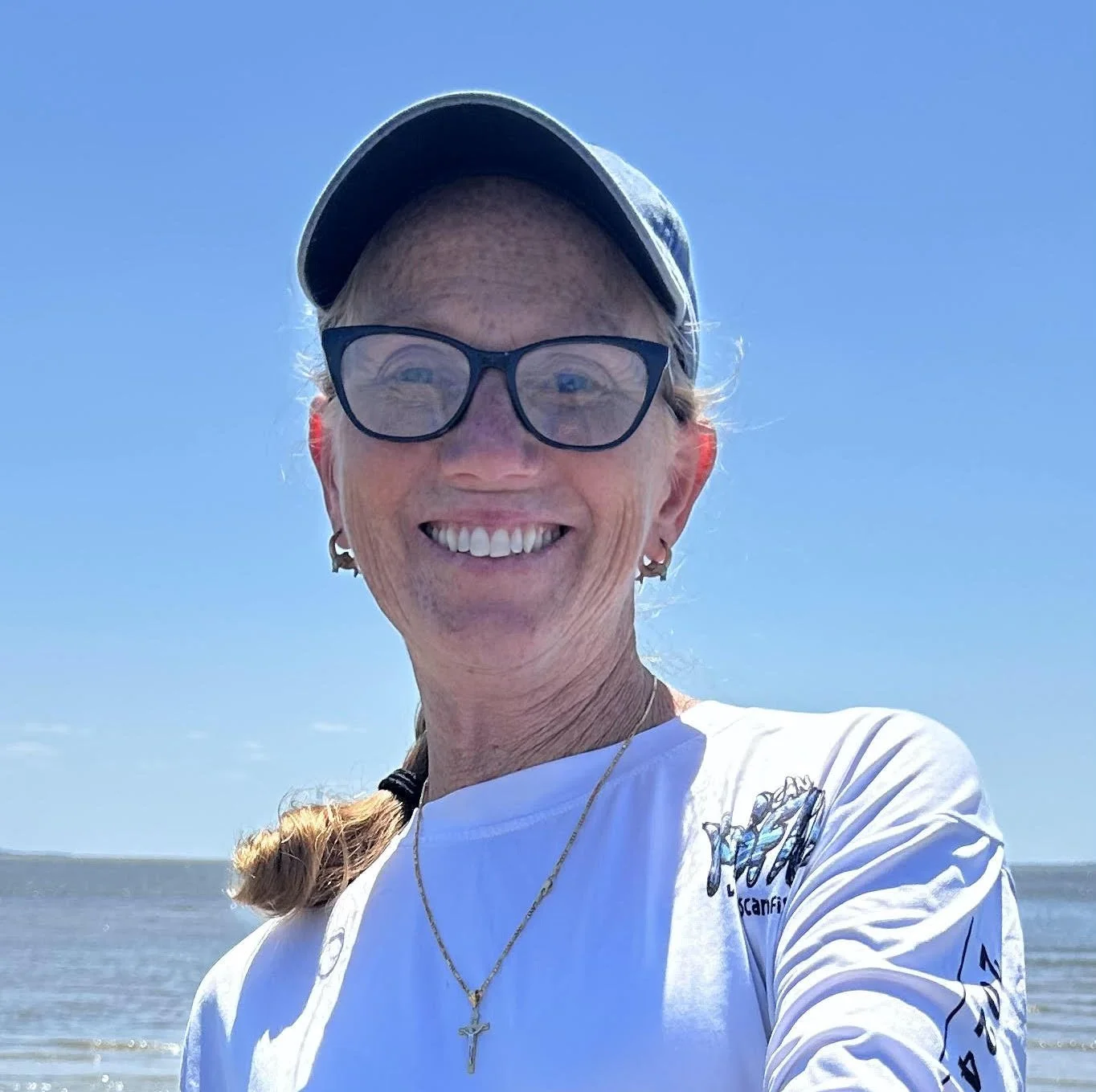 Woman wearing glasses and hat smiles at camera.