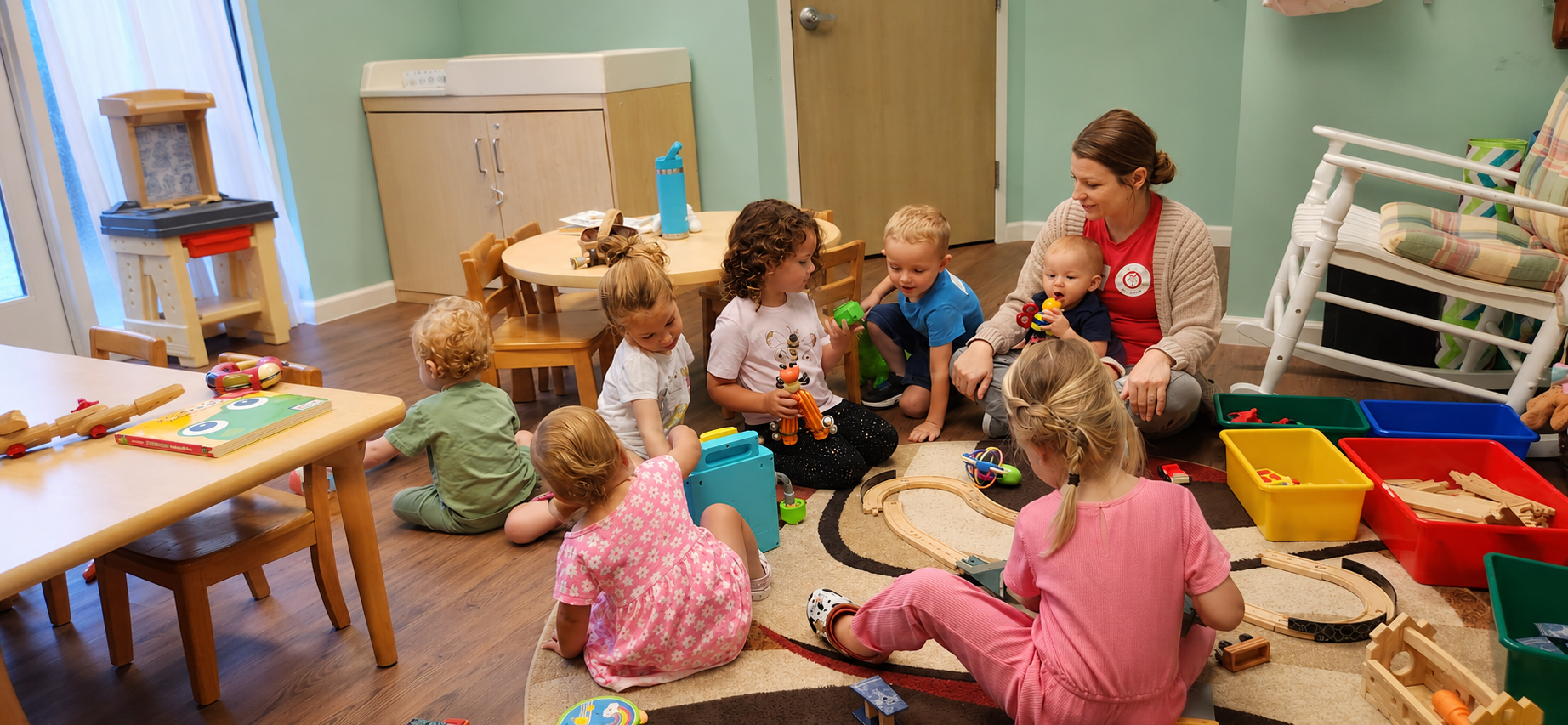 nursery students sit with teacher on a rug playing with toys.