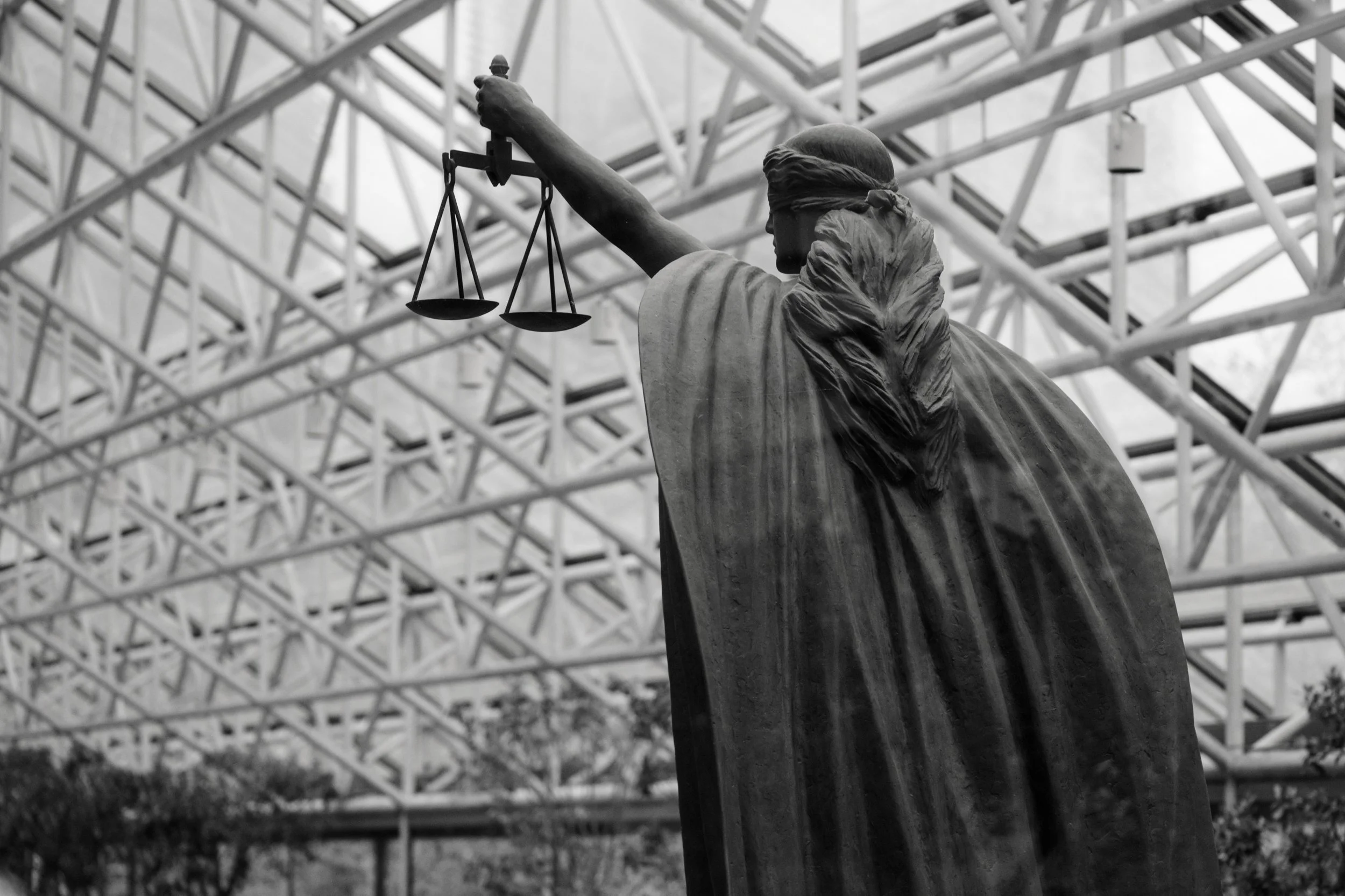 Close-up of Lady Justice statue holding scales, with a modern structural roof above.