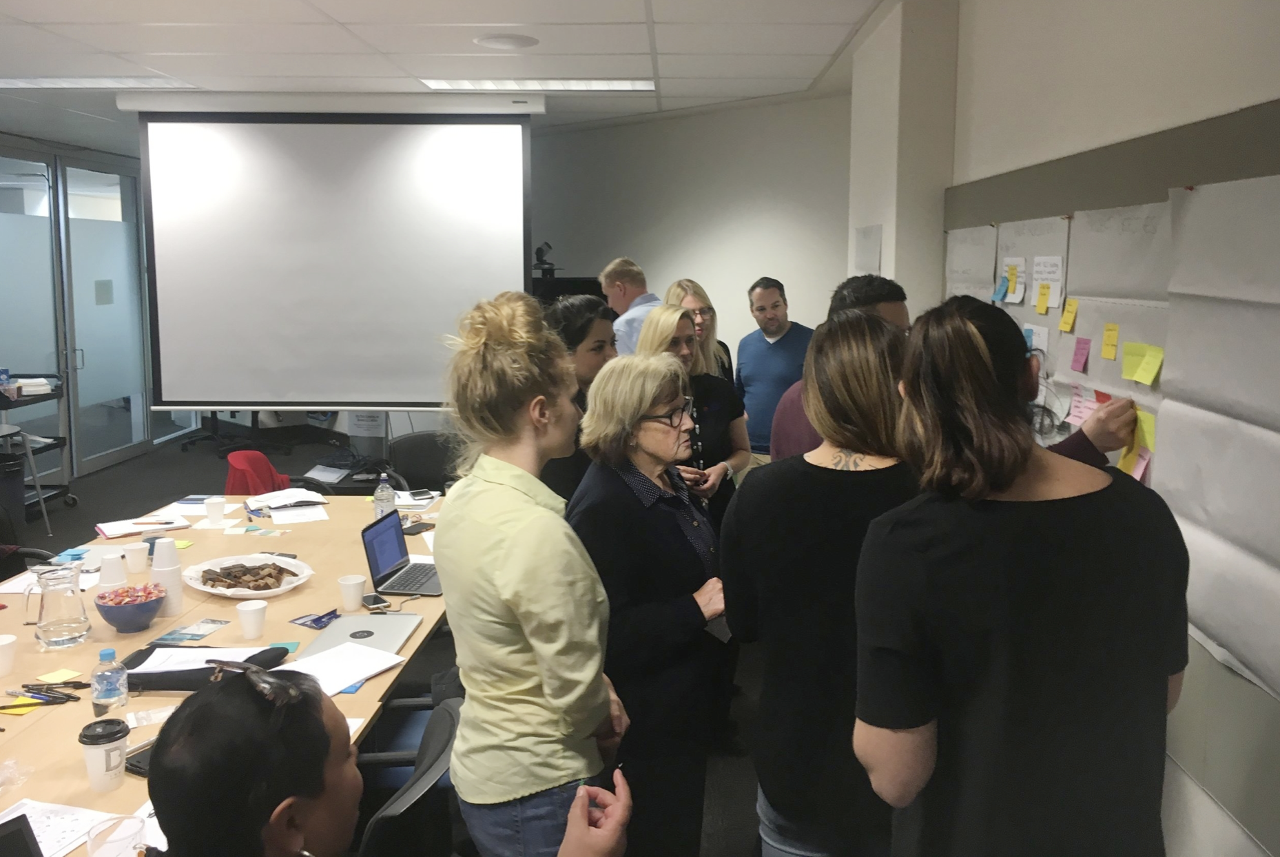 A picture of me, and a group of 10 DCJ clients huddled around a pin board. We are organising post-it notes.