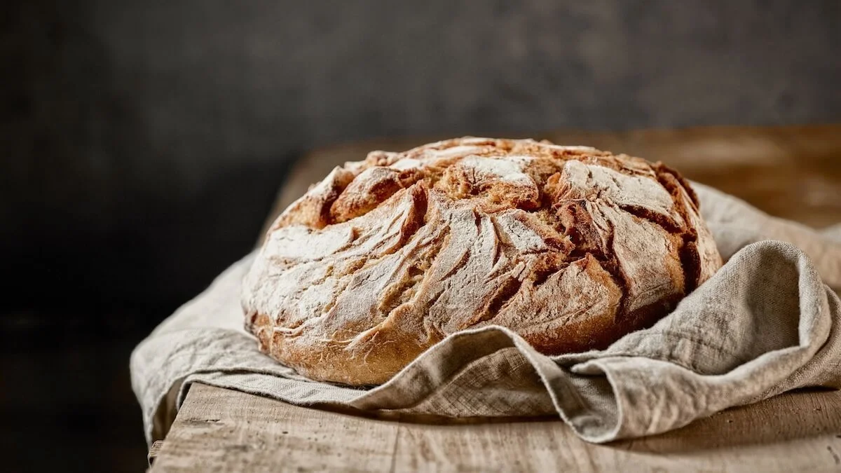 2026 Simple Home Favorites (Artisan bread round in natural cloth on wooden table)