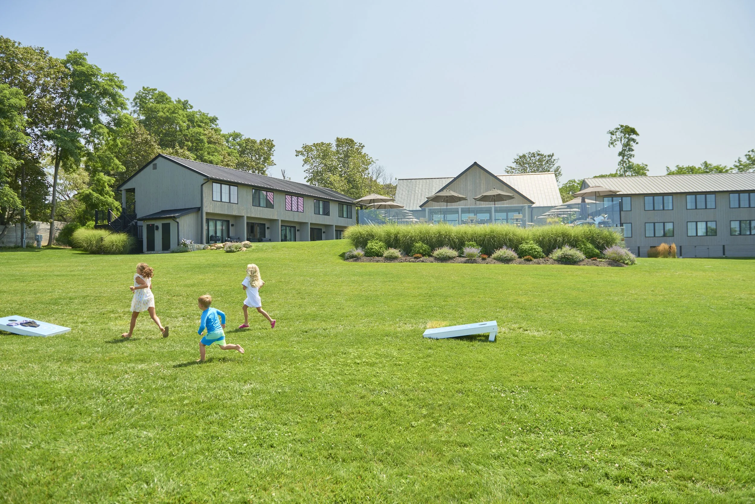 A scene of children playing on a vast green lawn at Hotel Moraine with the pool in the background
