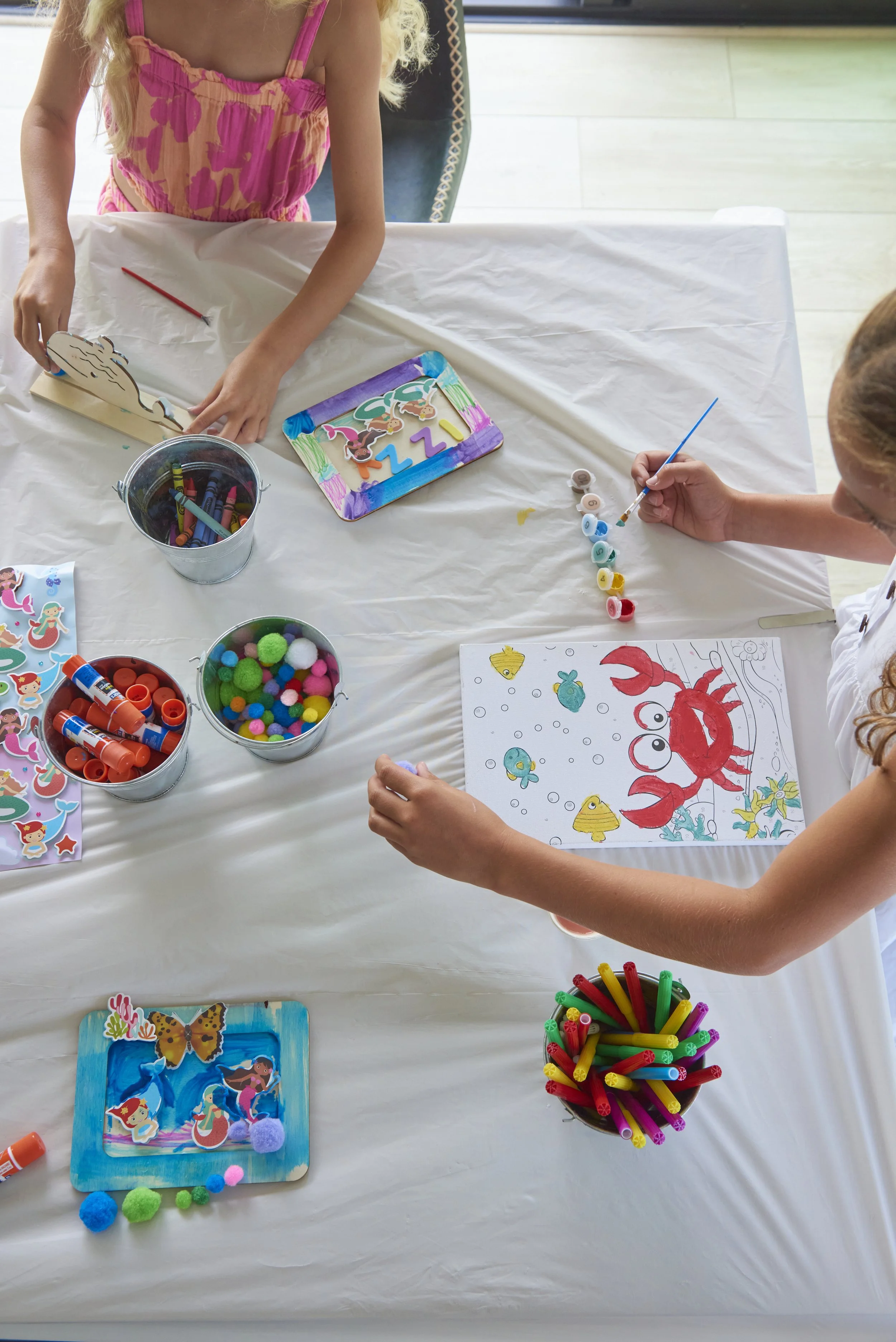 A spread of kids crafts on a white tablecloth with children painting