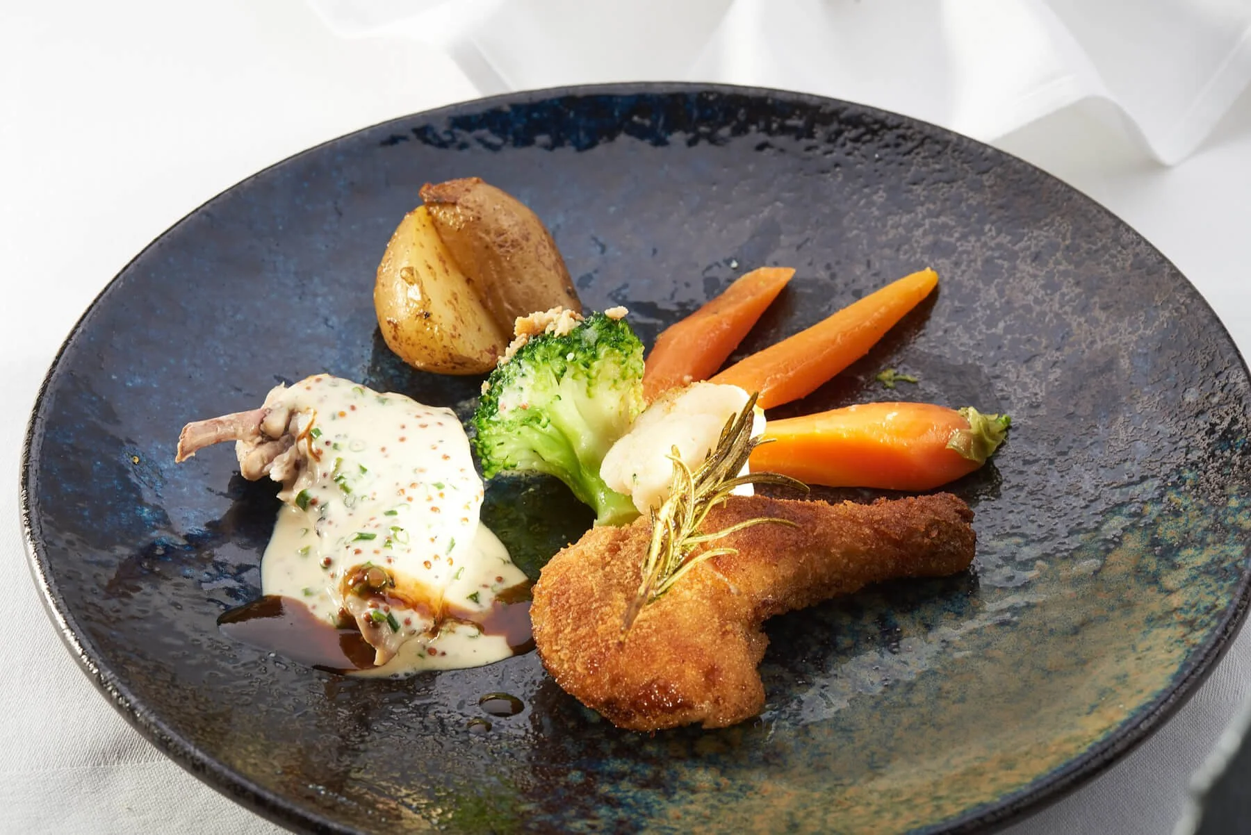 Gebratenes Hähnchenfilet mit Sauce, Kartoffeln, Brokkoli, Karotten und ein kleines Stück Fisch auf einem schwarzen Teller