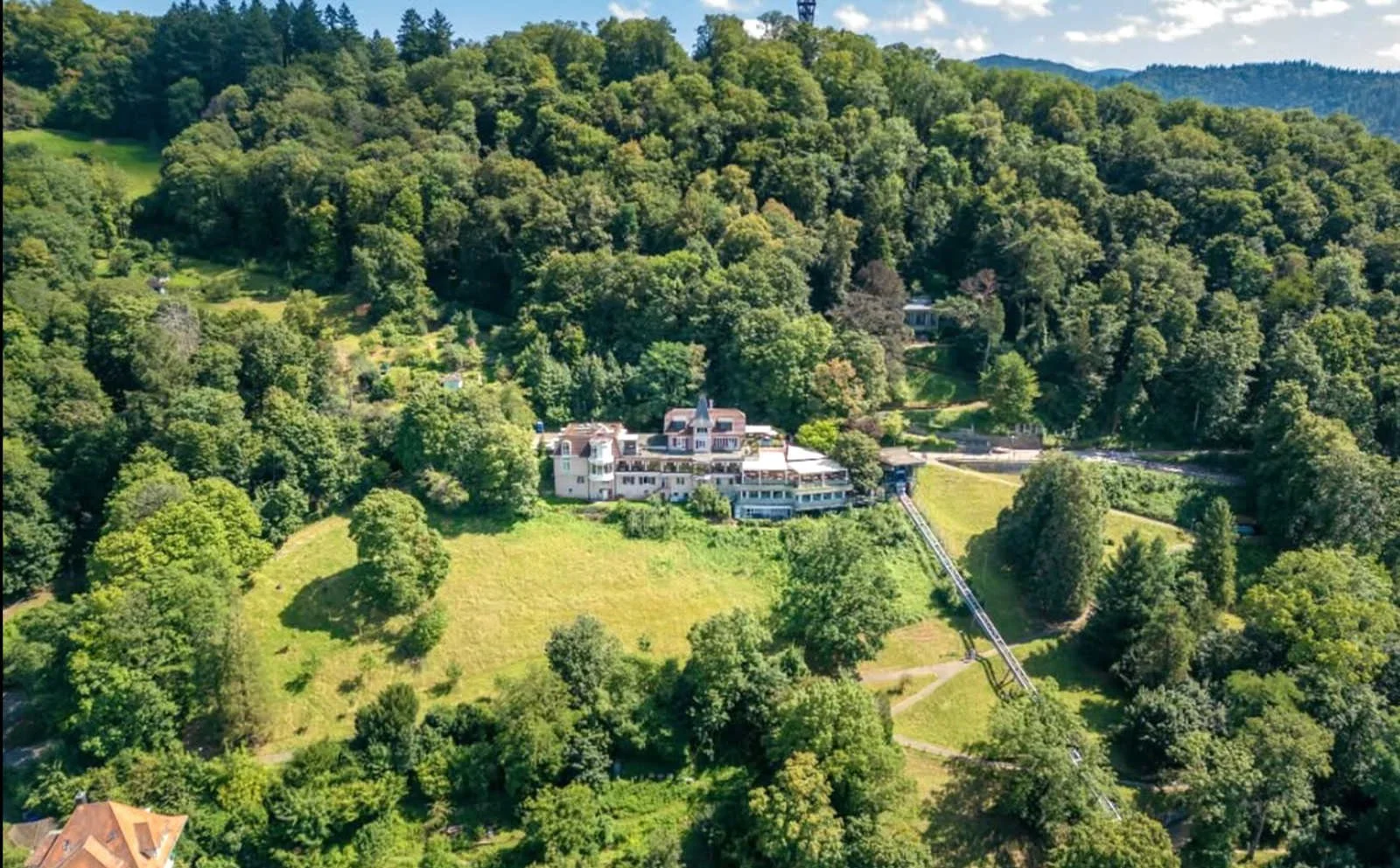 Ansicht des Dattler Schlossbergrestaurant auf dem Schlossberg Freiburg, umgeben von Bäumen, mit einer Seilbahn, die zum Restaurant führt.