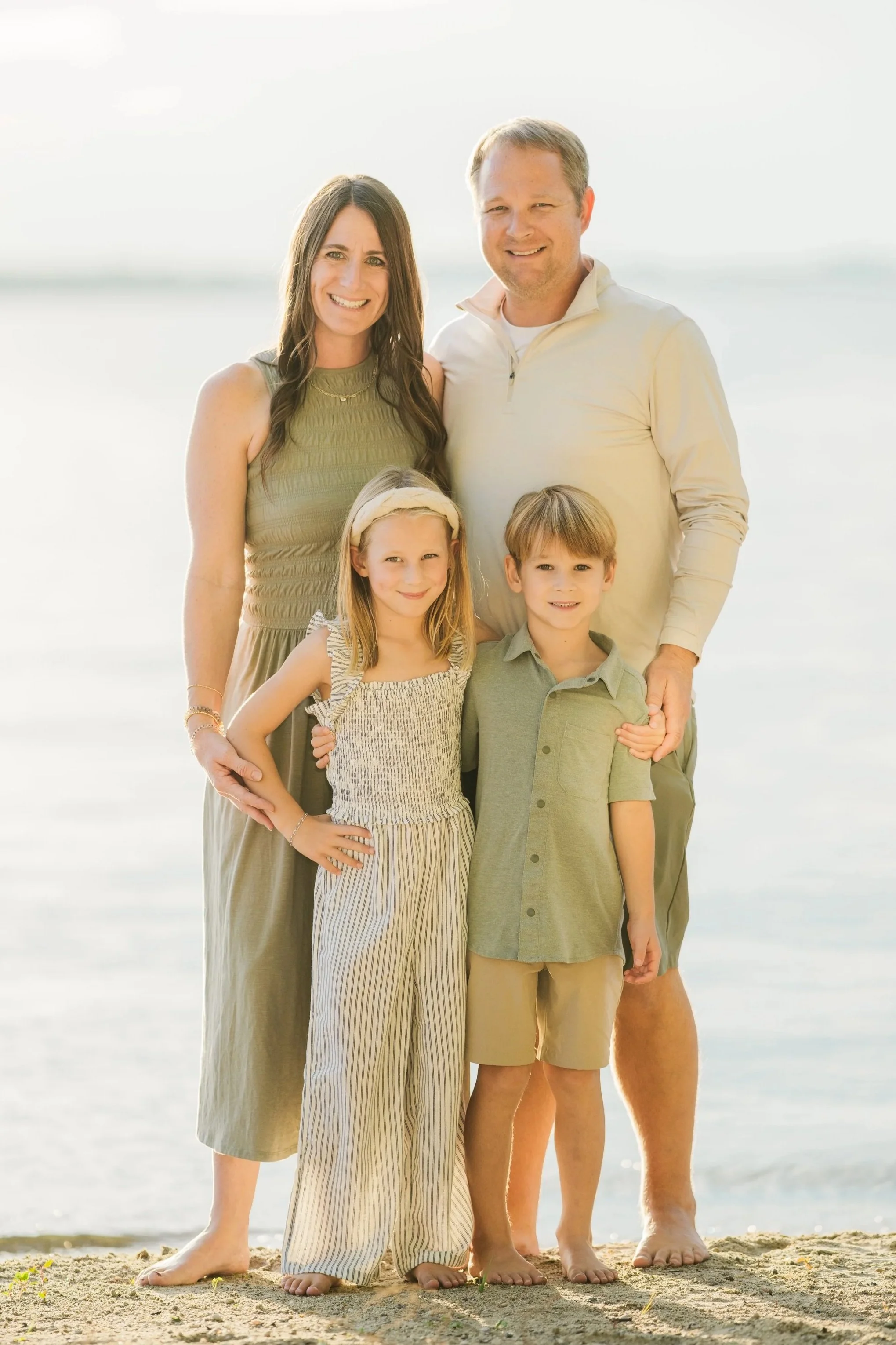 A family of five standing in a field during fall, smiling at the camera. The family includes a woman, a man, and three children.